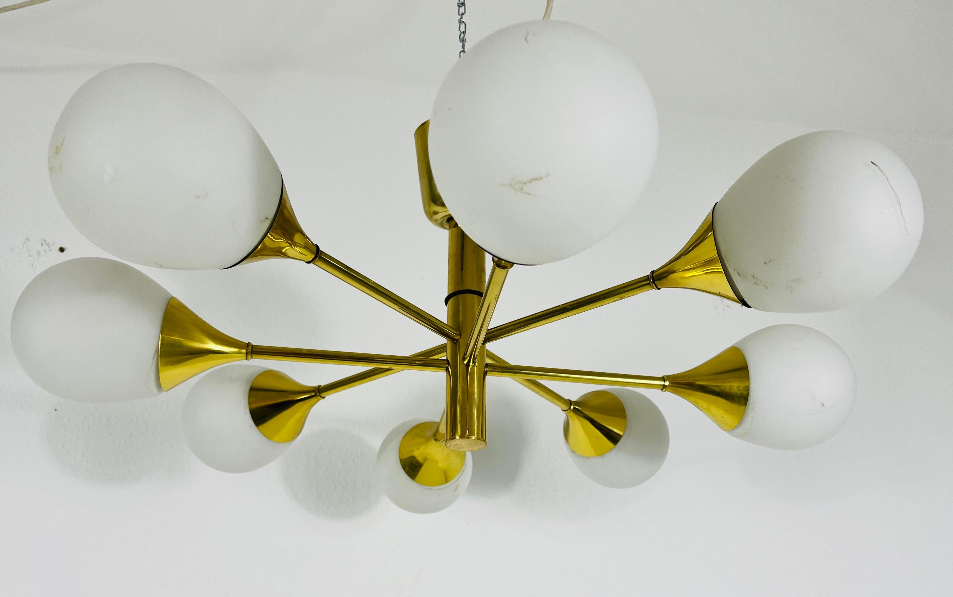 A midcentury chandelier by Kaiser Leuchten made in Germany in the 1960s. It is fascinating with its Space Age design and eight opaline glass balls. The circular body of the light is made of polished brass, including the arms. 

Good vintage