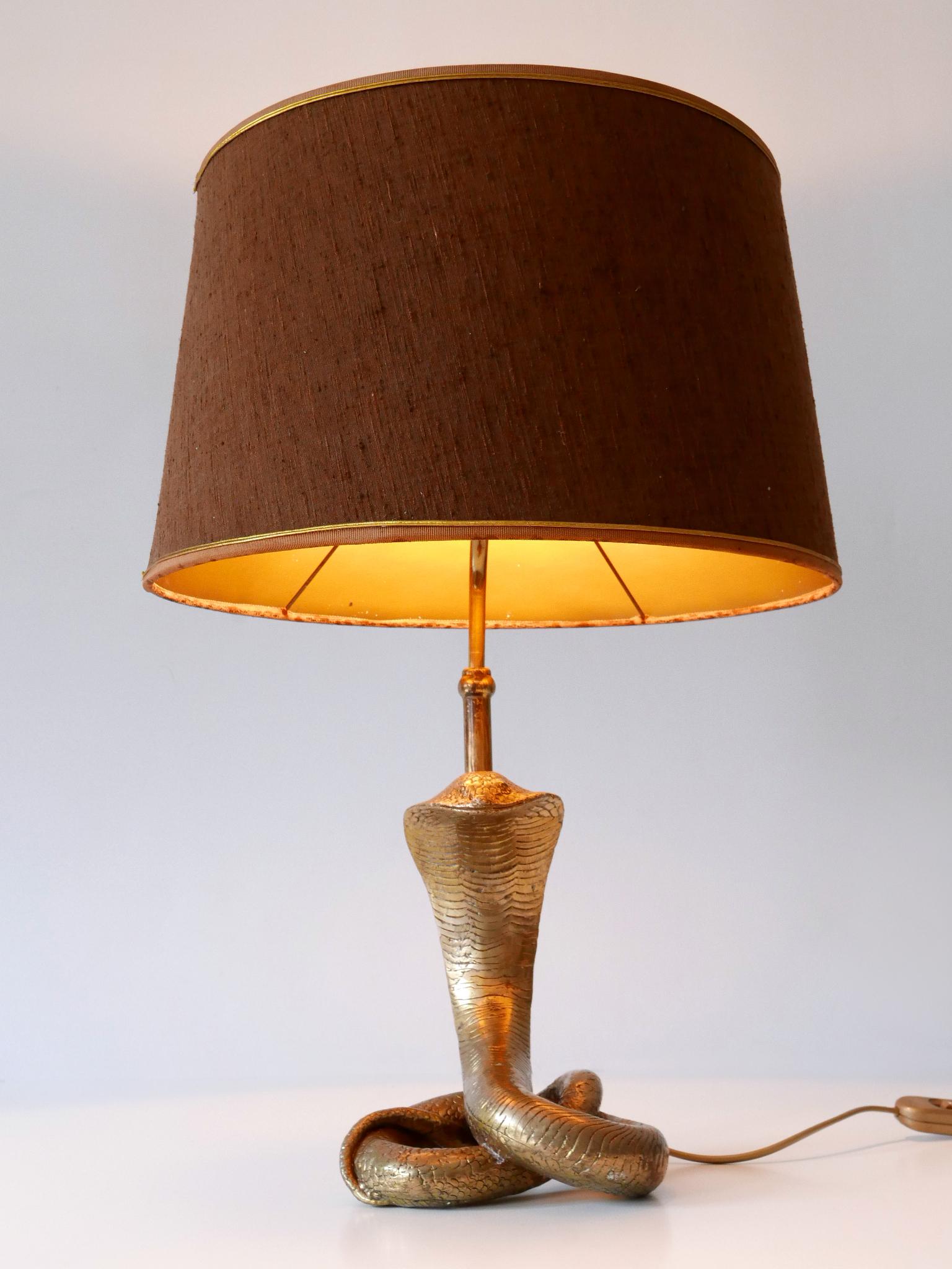 Extraordinary and amazing Mid-Century Modern brass 'cobra' table lamp. Designed & manufactured probably by Maison Jansen, France, 1970s.

Executed in massive brass, tube and silk/fabric shade, the lamp comes with 1 x E27 / E26 Edison screw fit bulb