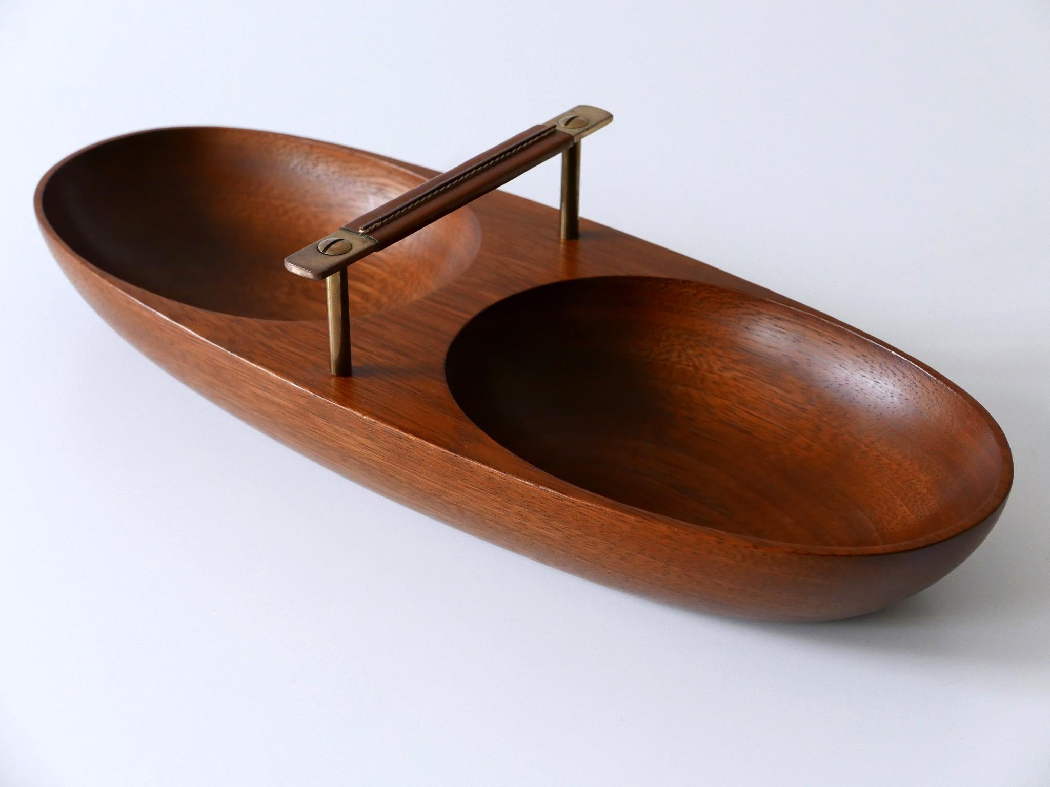 Extremely rare and elegant Mid-Century Modern nut bowl by Carl Auböck II, Vienna, Austria, 1950s.

Executed in solid teak wood and brass handle upholstered in leather.

Dimensions: 
W 15.36 in. (39 cm)
D 5.91 (15 cm)
H 3.86 (9.8 cm)

Good