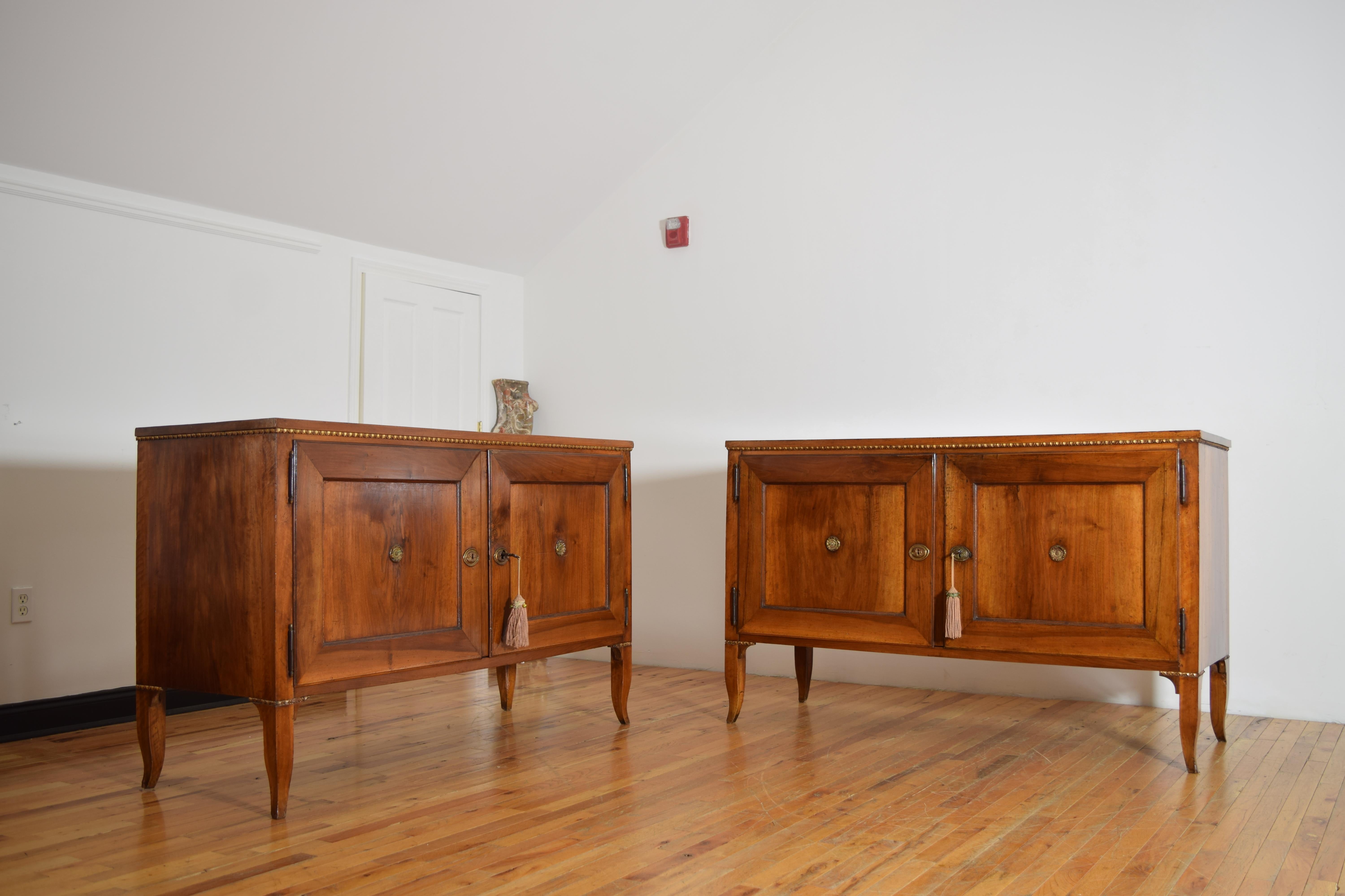 a rare pair of period walnut credenzas from the Veneto region of Italy, having rectangular tops with carved under-moldings atop conforming cases with two paneled doors retaining original hinges and brass medallions, raised on tapered cabriole legs