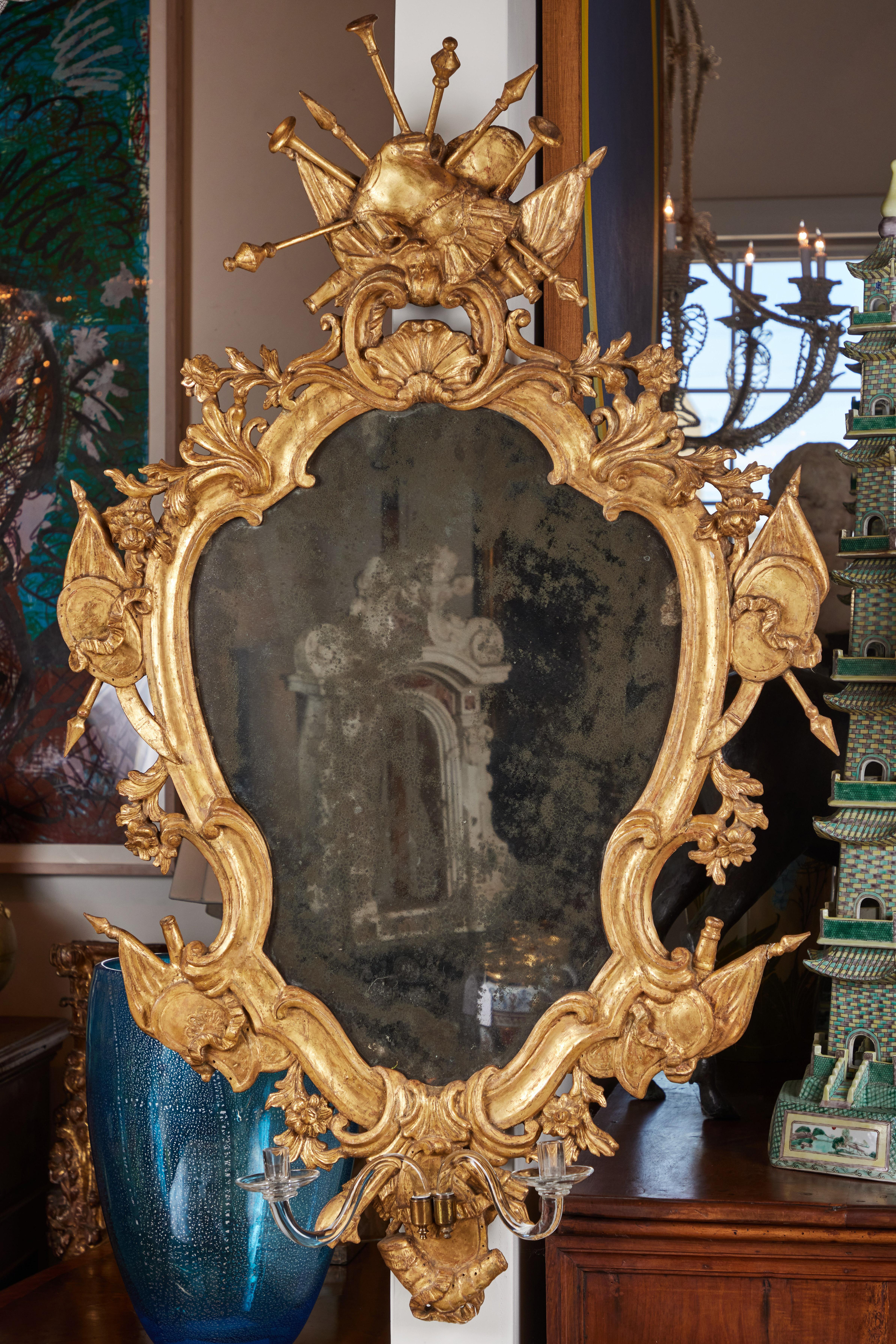 Paire de miroirs vénitiens de grande taille, entièrement originaux, sculptés à la main, gessés et dorés à l'or fin 22 carats, en forme d'écusson, présentant des reliefs feuillus, des drapeaux et des couronnes dramatiques composées d'armures de