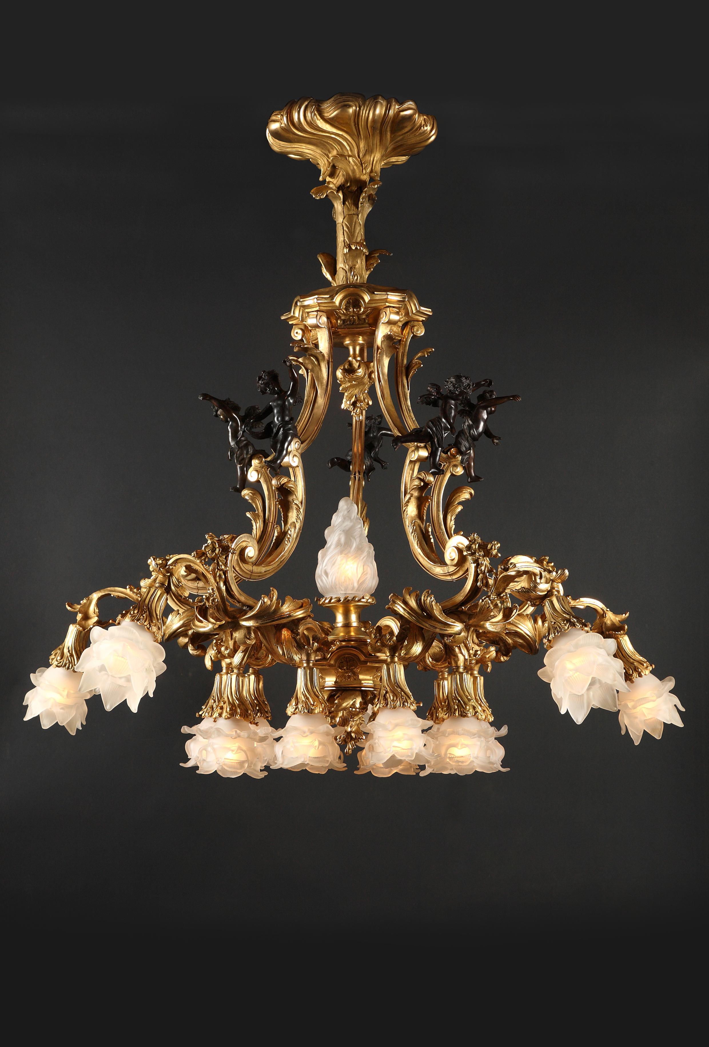 A sumptuous pair of 16 lights gilded bronze chandeliers attributed to T. Millet, ornamented with Louis XV style motifs, such the five patinated putti under an architectural structure, surmounting the foliated scrolled light arms and their flower