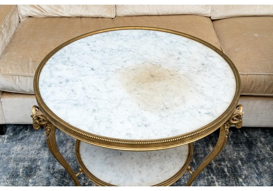 Une extraordinaire paire de tables de Guéridon de style Louis XVI en bronze doré, avec des plateaux circulaires en marbre blanc et des étagères inférieures ouvertes. Elle repose sur des tripodes de pieds en sabre avec d'élégants et détaillés