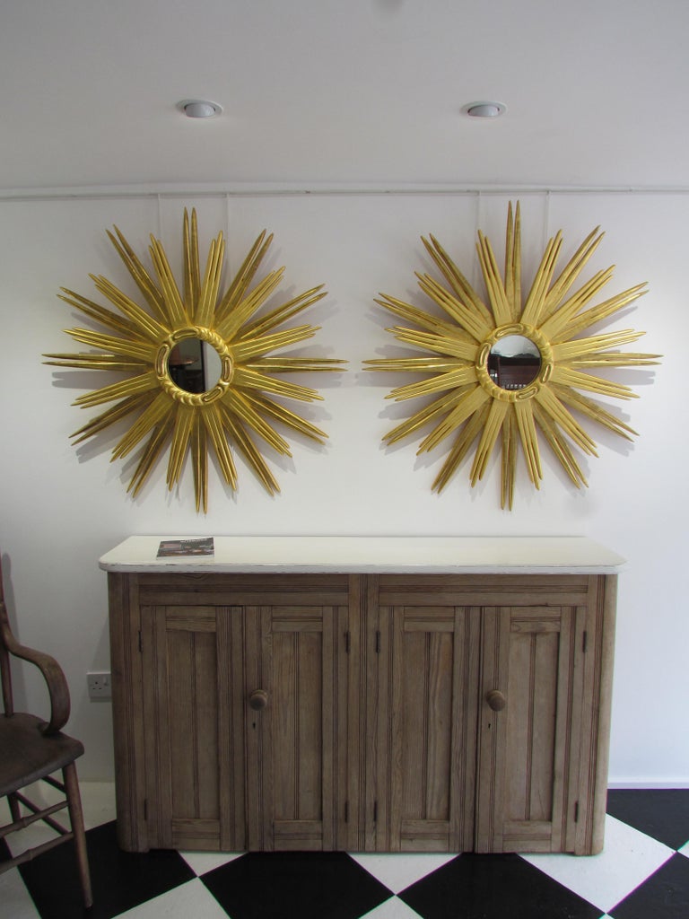 An exceptional pair of large scale hand carved and 23.75 carat gold gilt sunburst mirrors in the Art Deco style. Period antique mirror glass.