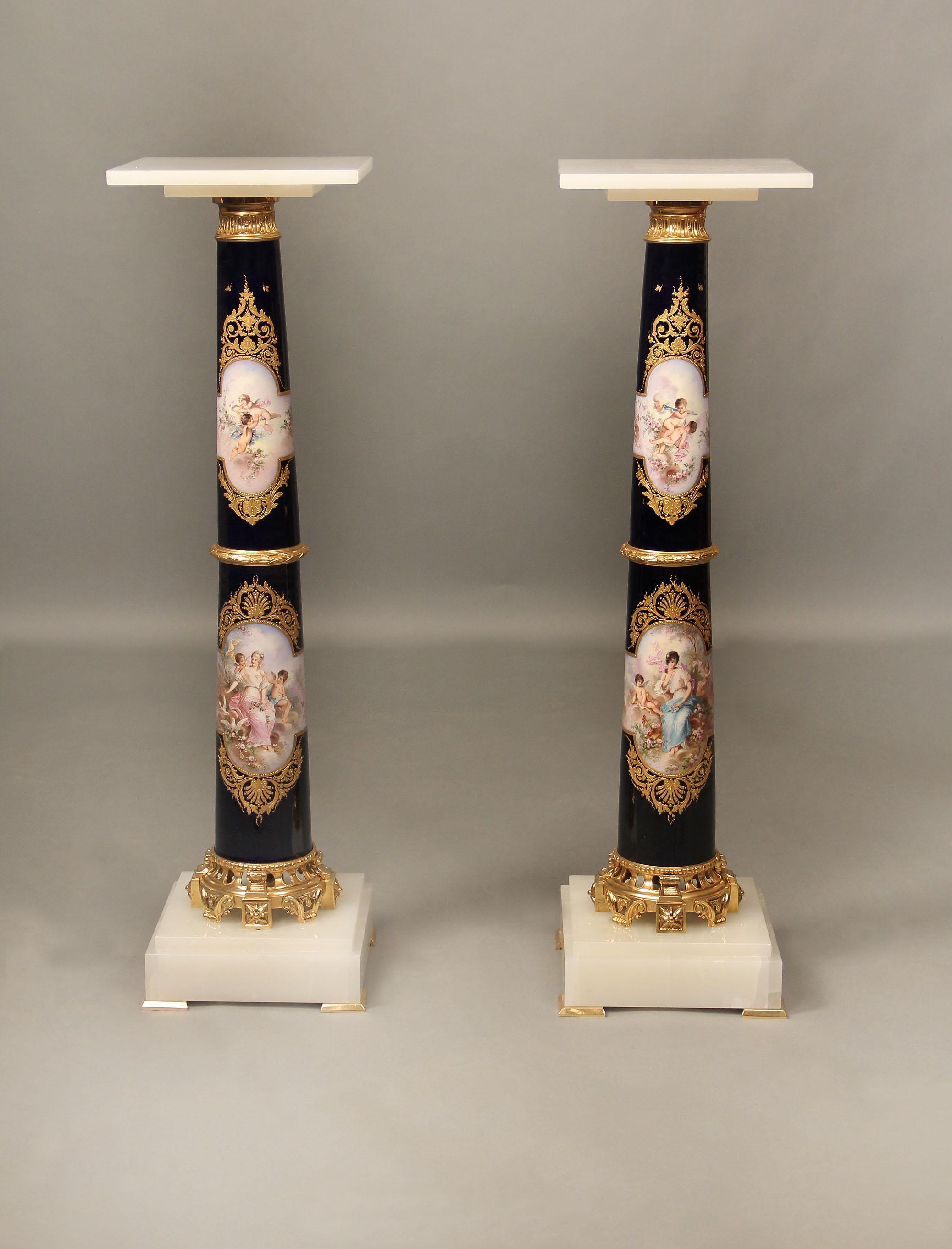 Exceptionnelle paire de piédestaux en bronze doré montés en onyx et de style Sèvres, datant de la fin du XIXe siècle

Plateau carré en onyx surmontant un support en forme de colonne peint de charmantes scènes de femmes et de chérubins, les dos