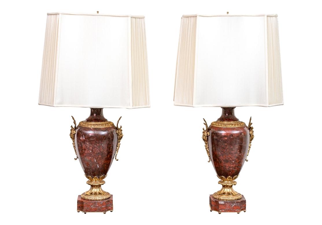 Notable Pair of Urn form Table Lamps in Neoclassical  style  with good size and great weight. The stone in an Oxblood Porphyry with  fine color and Classical brass mounts including Masks and Foliate details with the Porphyry bases having brass trim.