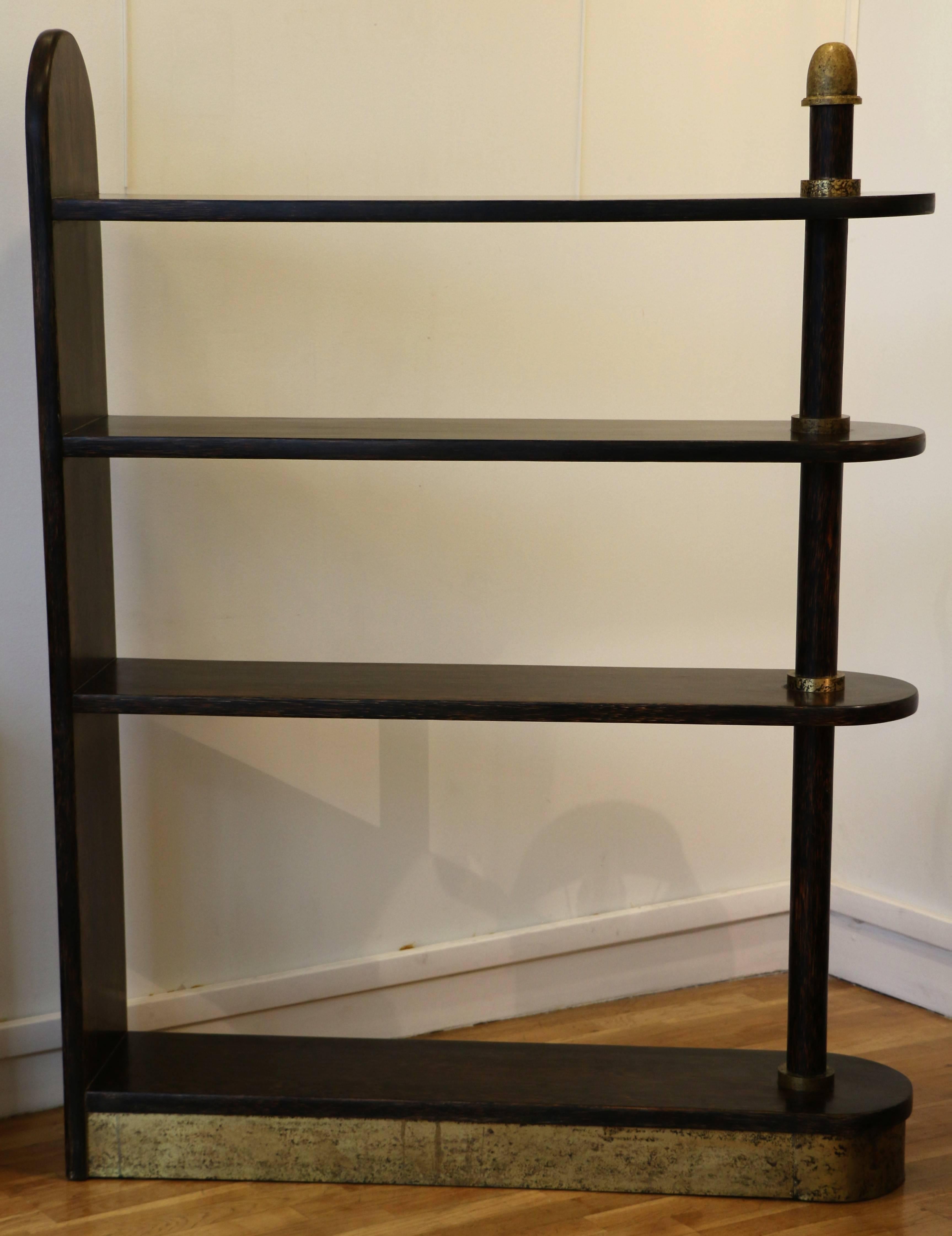 Bookcase from the 1930s by Eugène Printz (1889-1948). This exceptional bookcase is assymetrical and has four shelves. It is covered with palmwood veneer and has oxidized brass ornaments. Signed: Circular plaque marked 