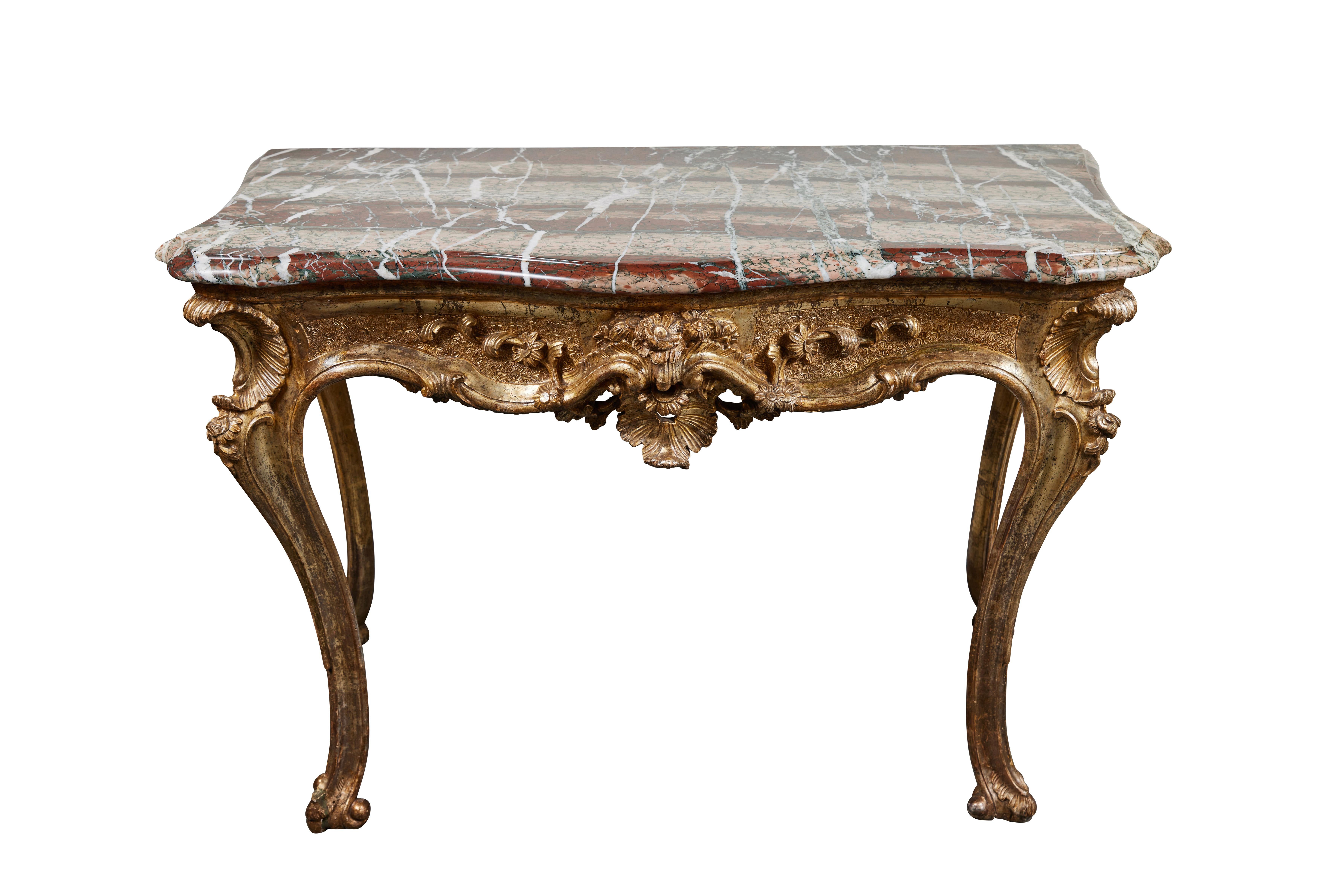 A pair of 18th century, hand-carved and champagne gilded, serpentine consoles surmounted by striking, original, polished marble tops. Each on long, graceful legs terminating in scroll-form feet. Each with four scooped corners, and dramatic aprons