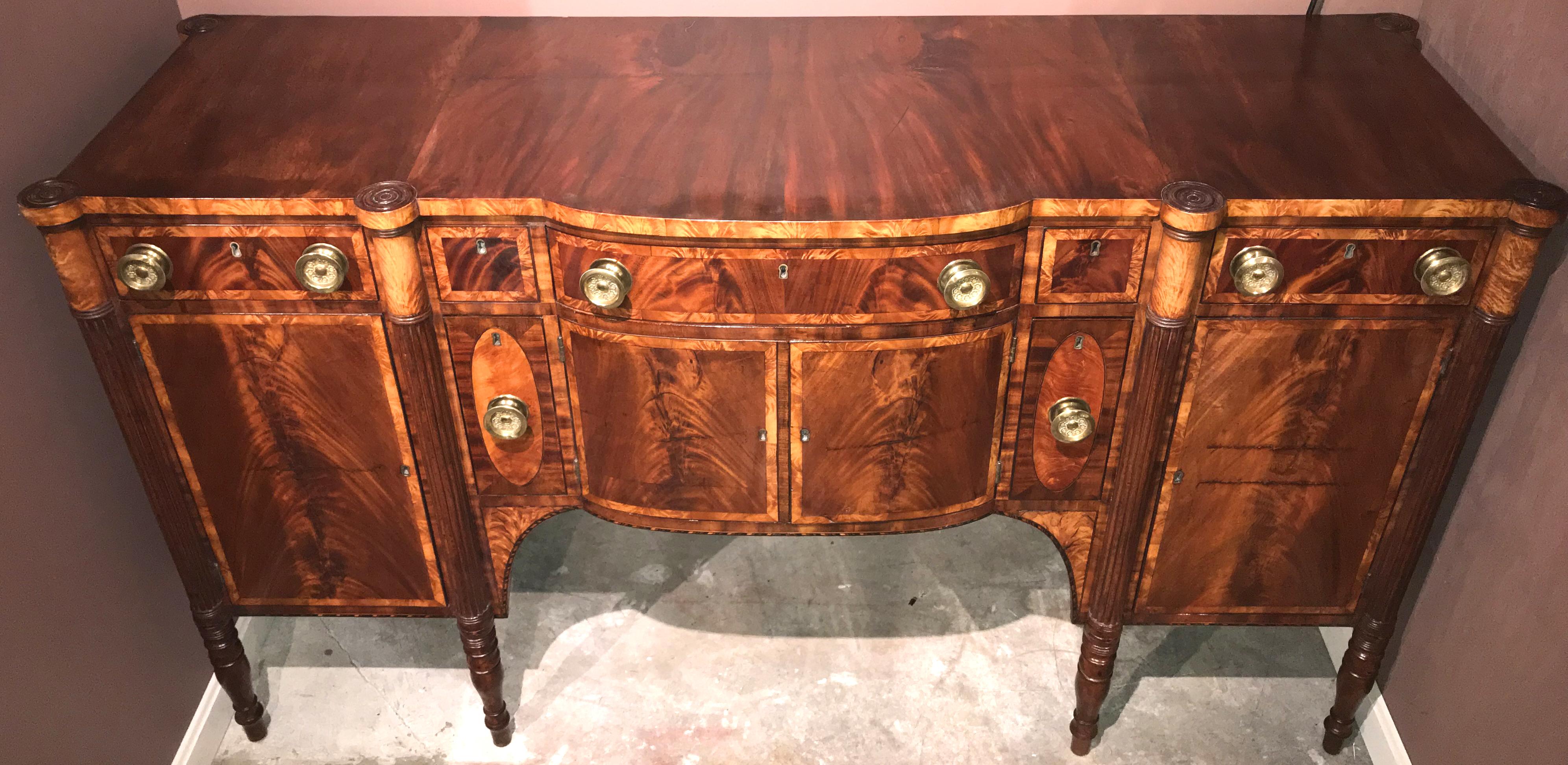 An exceptional Federal sideboard with bow front center section, conforming top surmounting an upper section with a center frieze drawer flanked by two fitted small drawers and two end drawers over two center doors, which open to interior storage,