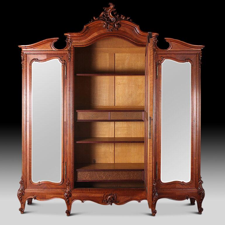 An exceptional-quality French carved walnut Louis XV three-door armoire, the three doors with their original shaped hand-beveled mirrors, the case profusely accented with very finely-carved details throughout. The doors open to reveal a