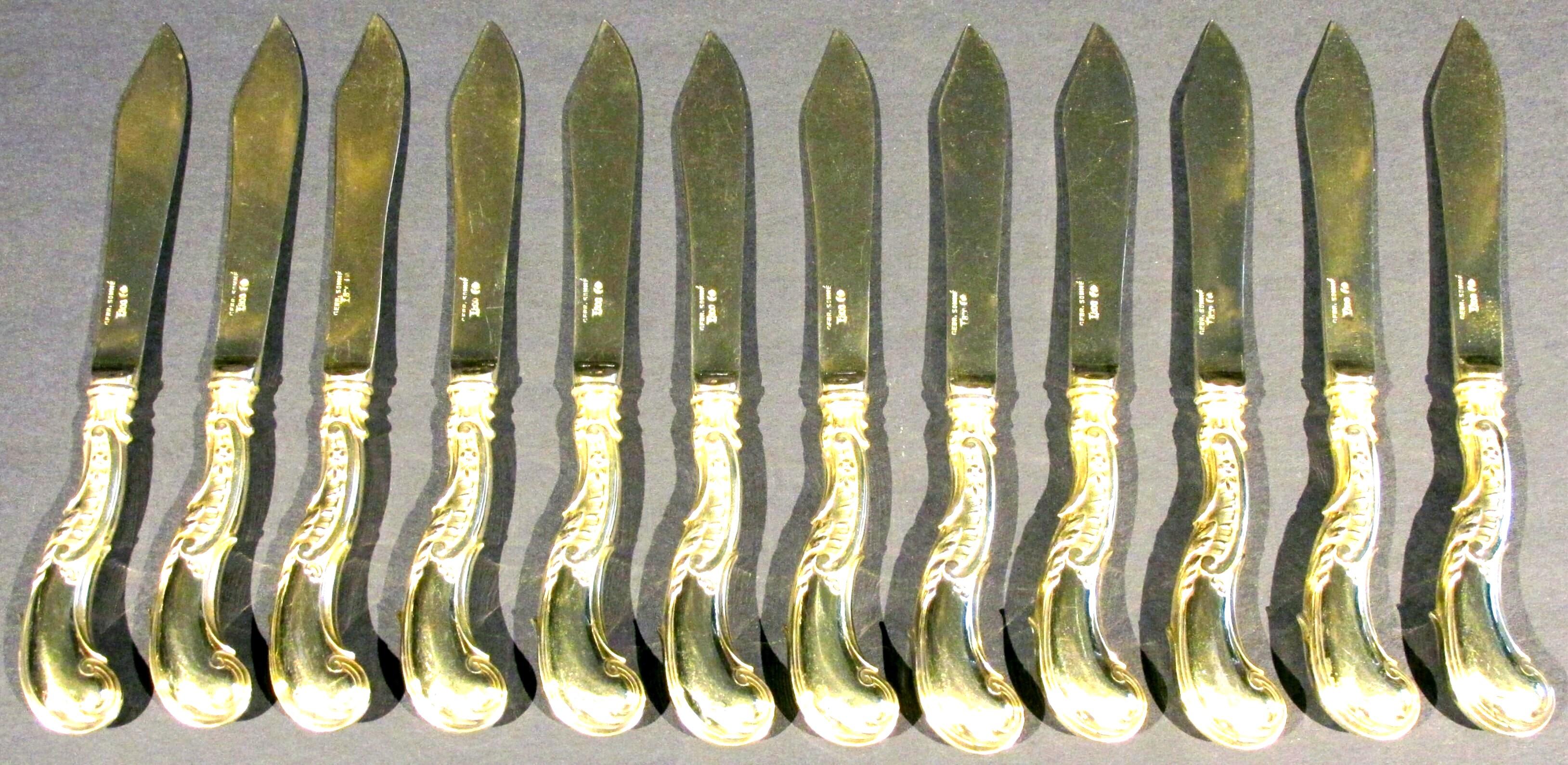 An exceptionally fine set of twelve Art Nouveau Period silver-gilt fish knives, all having richly cast and hand chased rocaille silver handles & blades with conforming scrolled and stippled detail, exhibiting a lustrous gilded surface overall. Each
