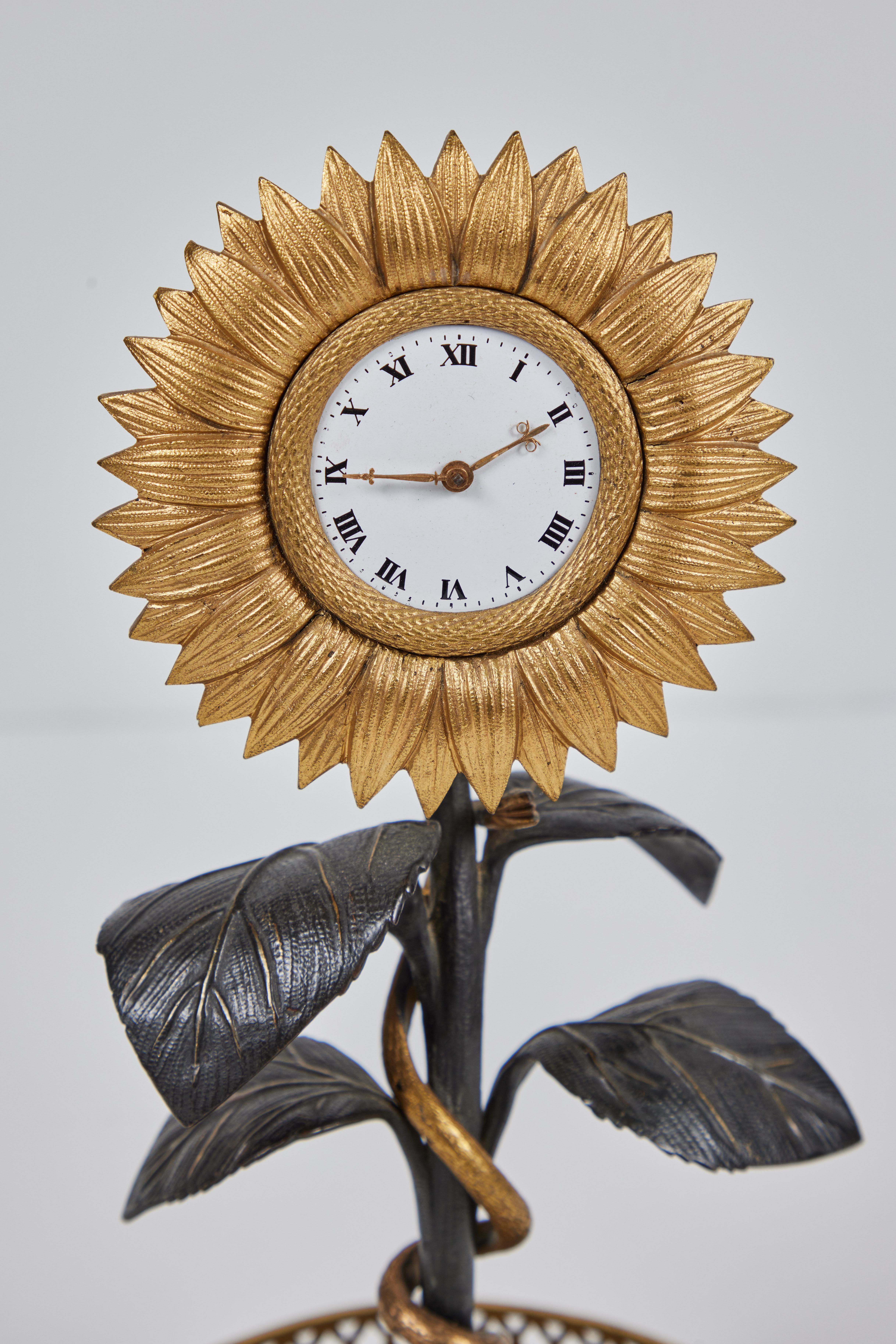 An extraordinary, period Restoration, ormolu and bronze sunflower timepiece, c. 1825. The clock set amidst radiant petals atop a curved stalk fitted with patinated bronze leaves, and surrounded by a delicate, gilded serpent above a faux planter with