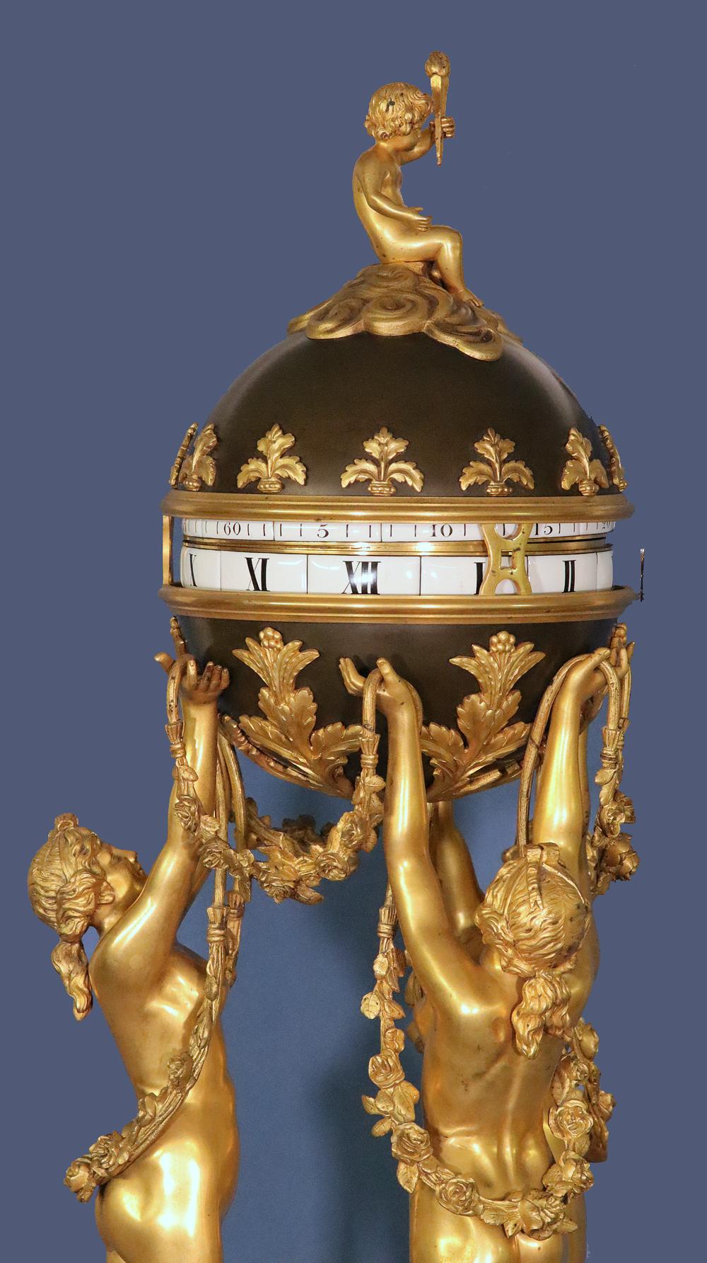The large exceptional gilt-bronze case depicts the ‘Three Graces’ draped in garlands supporting a large patinated sphere with a removeable top and adorned with decorative appliques and Cupid sitting amongst billowing clouds and holding a torch. They