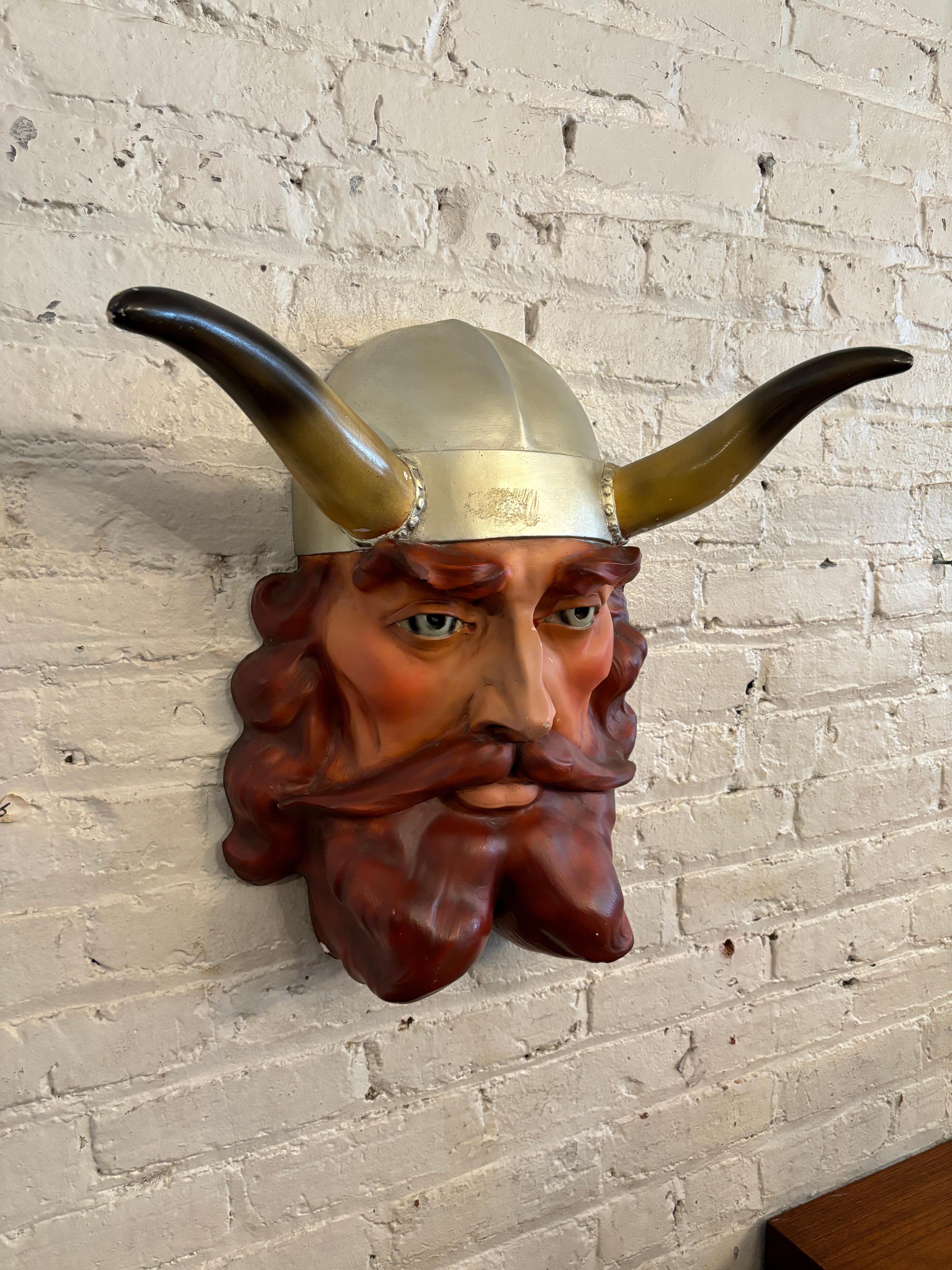 Bringen Sie einen Hauch von Geschichte und Skurrilität in Ihr Zuhause mit diesem charmanten, an der Wand montierbaren Wikingerkopf im Vintage-Stil! Die aus Gips gegossene Figur zeigt einen rotwangigen Wikinger mit rosigen Wangen, blauen Augen und