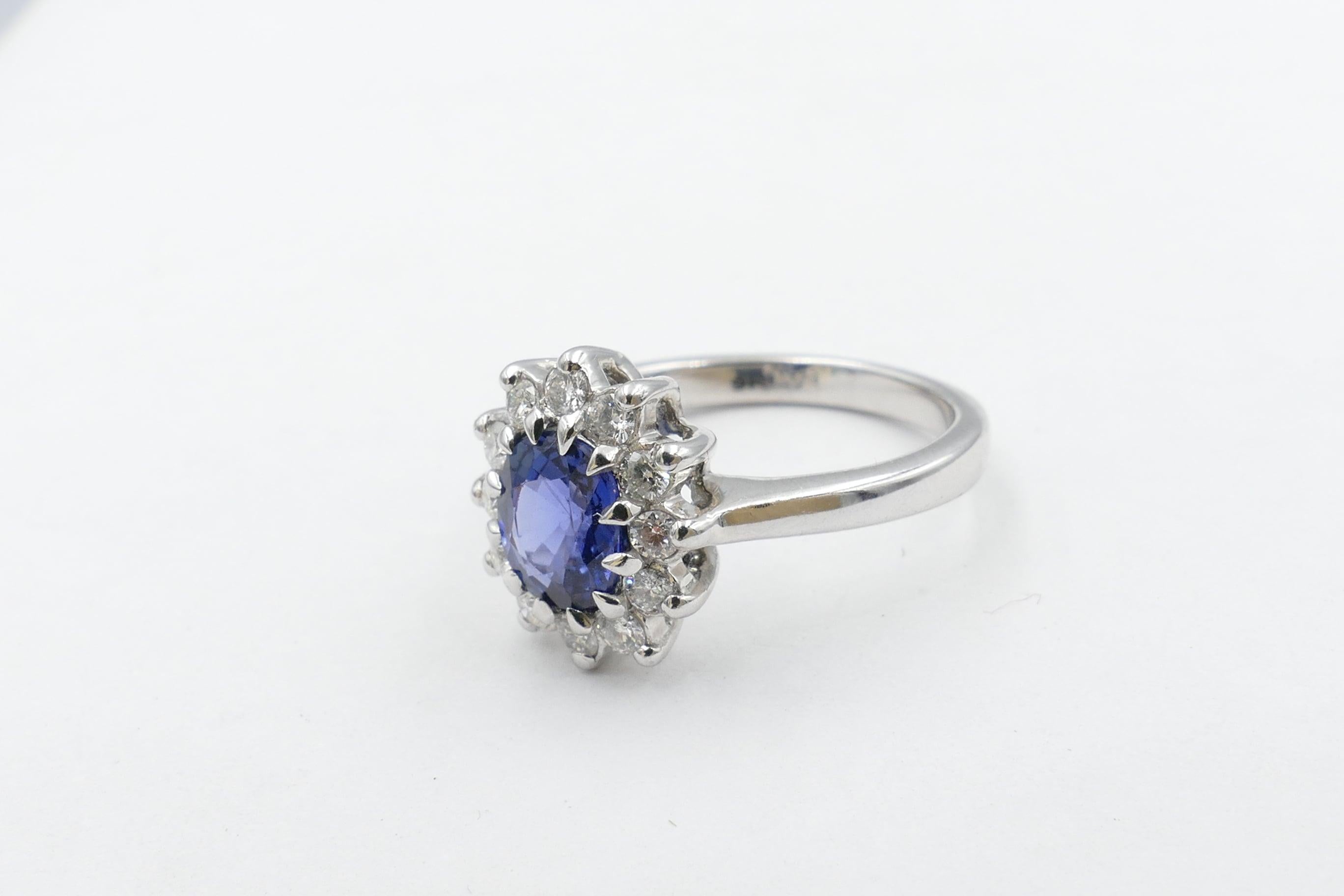 The 1.25 Carat Royal Blue, exceptional quality Sapphire is the centrepiece of this stunning Ring. It is Oval Cut, Clarity - eye clean, multi claw set, centering 12 Round Brilliant Cut Diamonds, bar/claw set, Colour G/H, Clarity SI1 - SI2 and