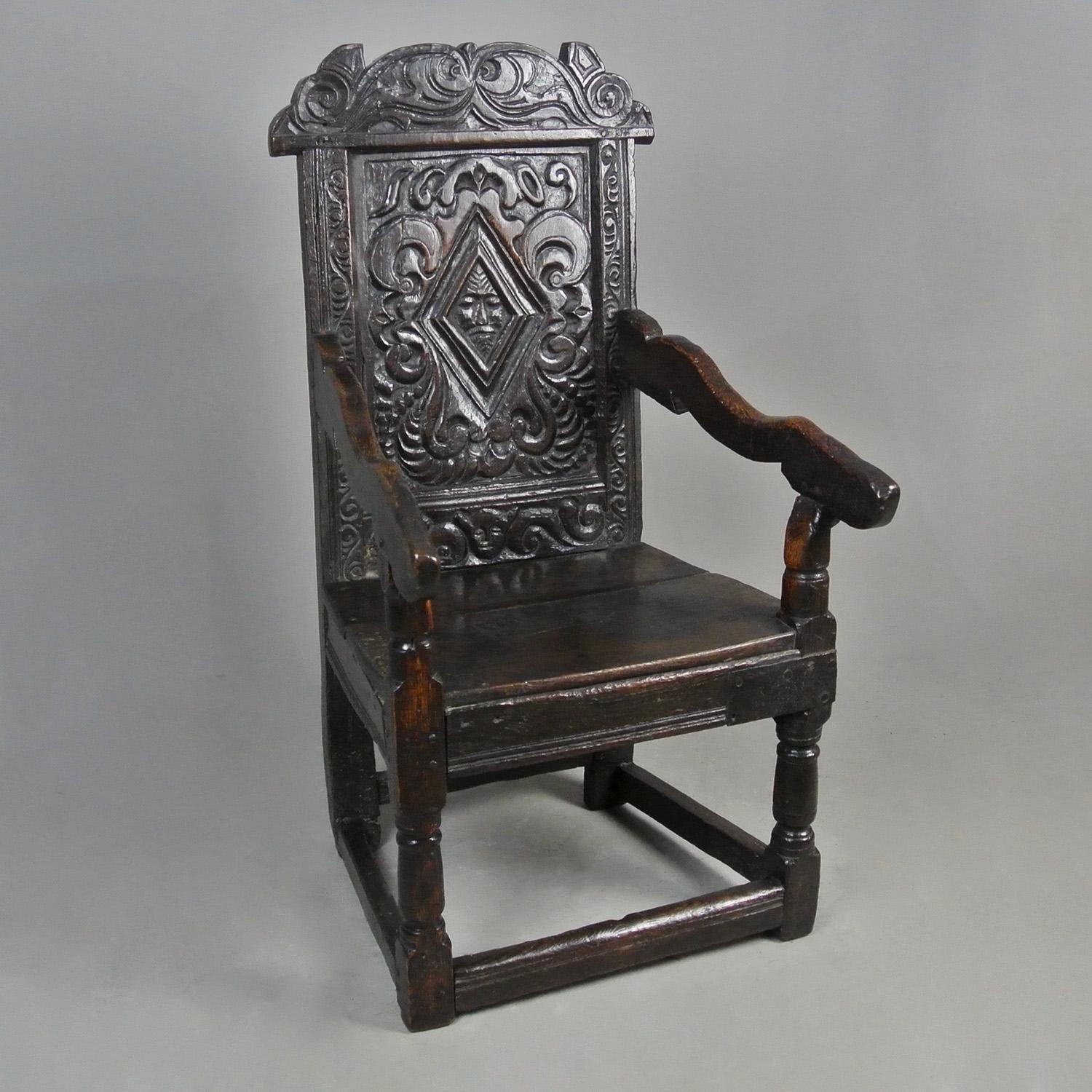 An extremely rare and exquisitely carved English oak wainscot chair dated 1609 and with two figural masks – the central mask possibly the ‘Green Man’ with foliage scrolling and falling around his face like hair or potentially a portrait of the