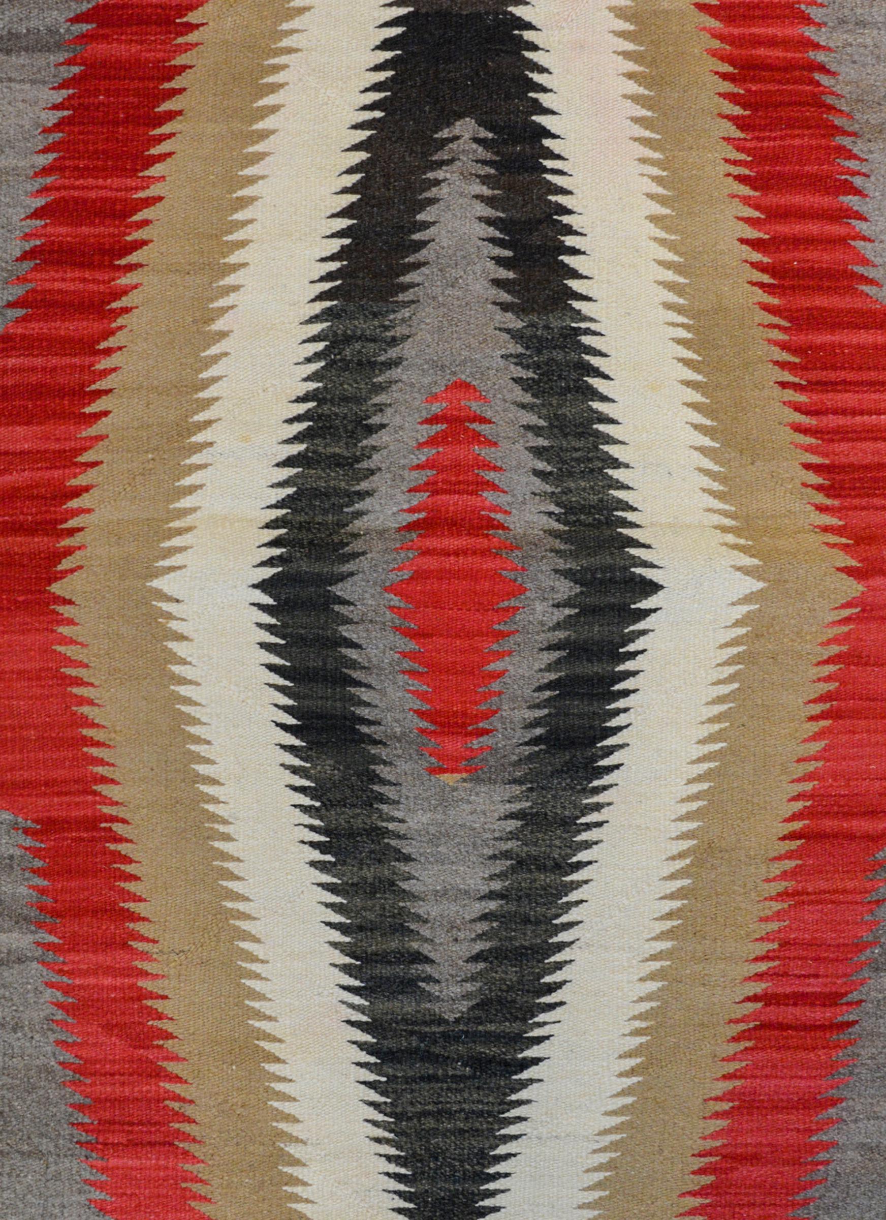 An exciting early 20th century Navajo rug with a beautiful radiating diamond pattern woven in crimson, gray, black, white, and tan wool surrounded by a solid white and black stripe border.