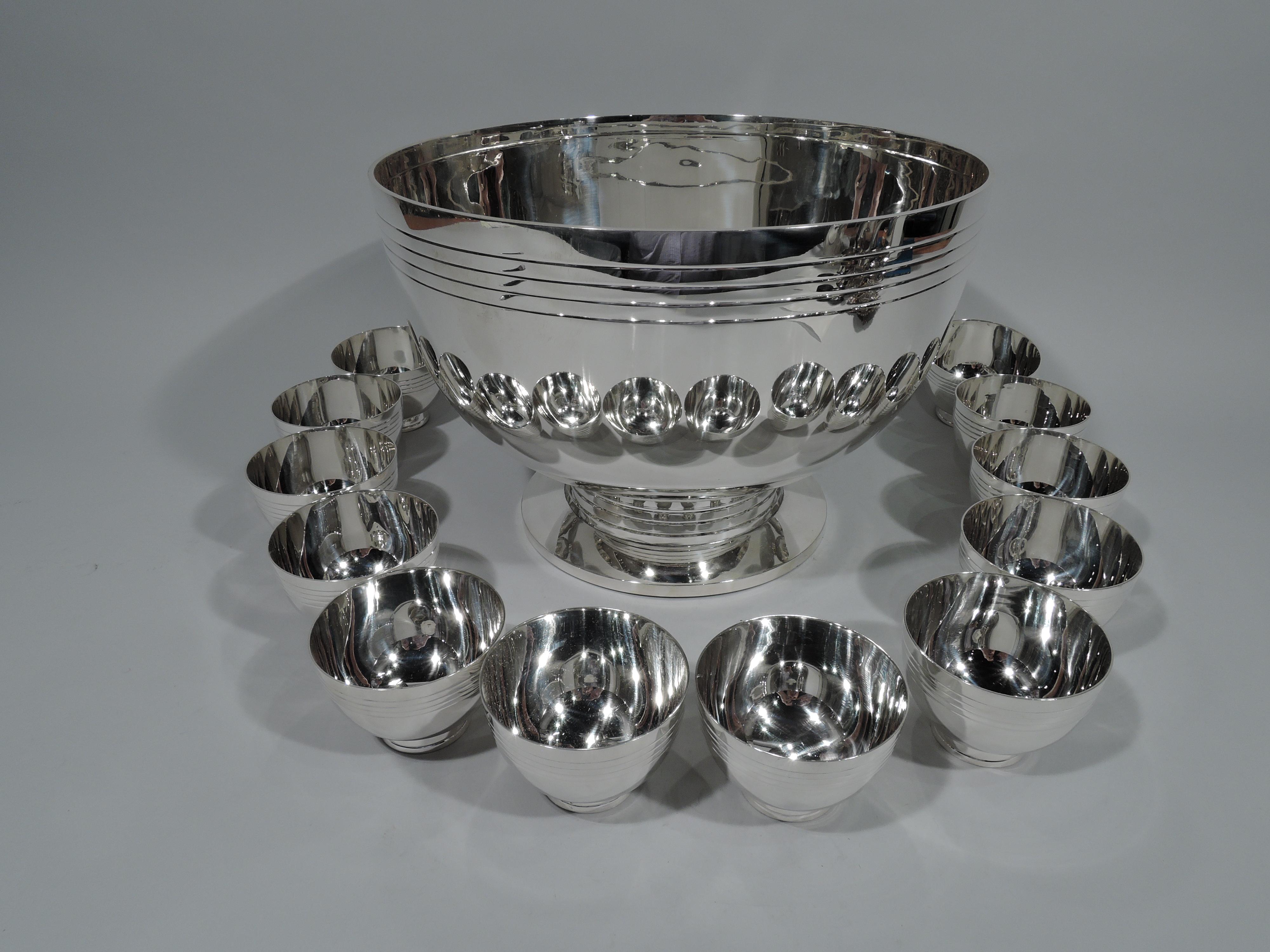 Exciting Mid-Century Modern sterling silver punchbowl and 12 cups. Made by Tiffany & Co. in New York. Punchbowl: Curved sides on inset support mounted to large and flat foot. Incised bands at rim and support. Each cup: Curved bowl on spread and