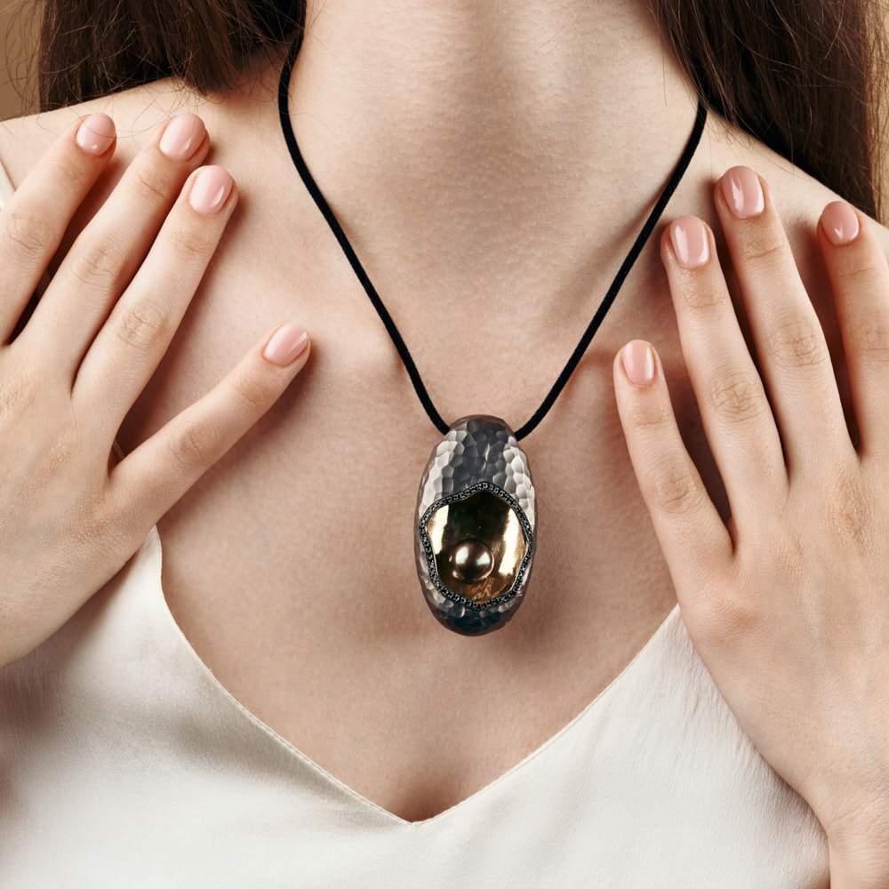 Nestled within the depths of this black rhodium pendant lies a mystical black pearl. Created as an exclusive one-off and uniquely special design, it offers a lining of precious metal as glistening black spinels trim around a beating hidden heart.