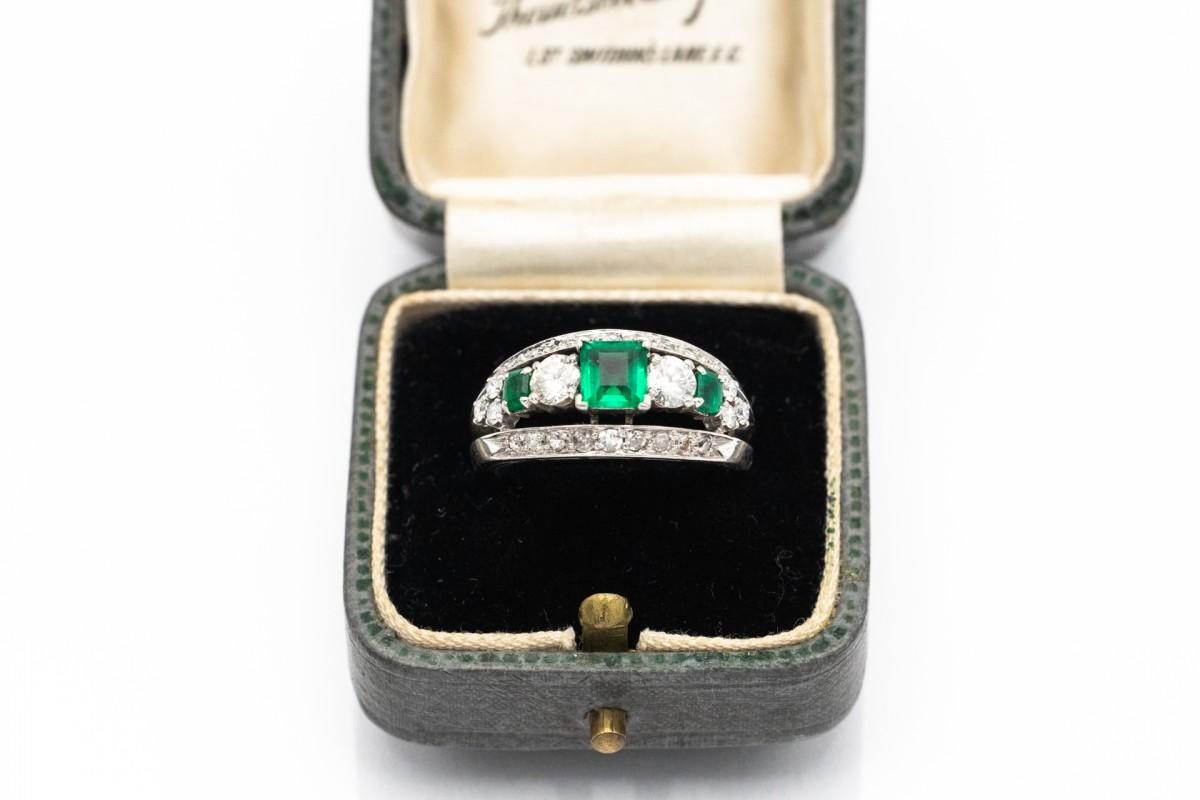 Unique ring in platinum, decorated with emeralds and diamonds, combining classic elegance with the subtle shine of precious stones. Its central point is a beautiful emerald with a deep, green color and a weight of about 0.50 ct. On the sides there
