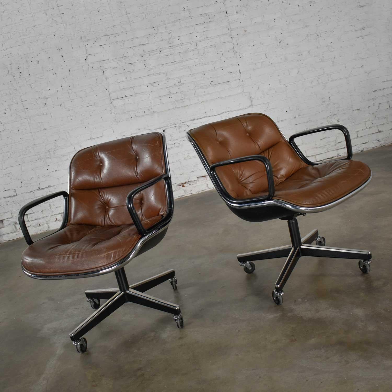 Fabulous pair of executive armchairs by Charles Pollock for Knoll. Comprised of brown leather, aluminum bands, painted black shafts, black plastic arms, and 4 prong bases. One chair is in wonderful condition with a little less overall wear, both