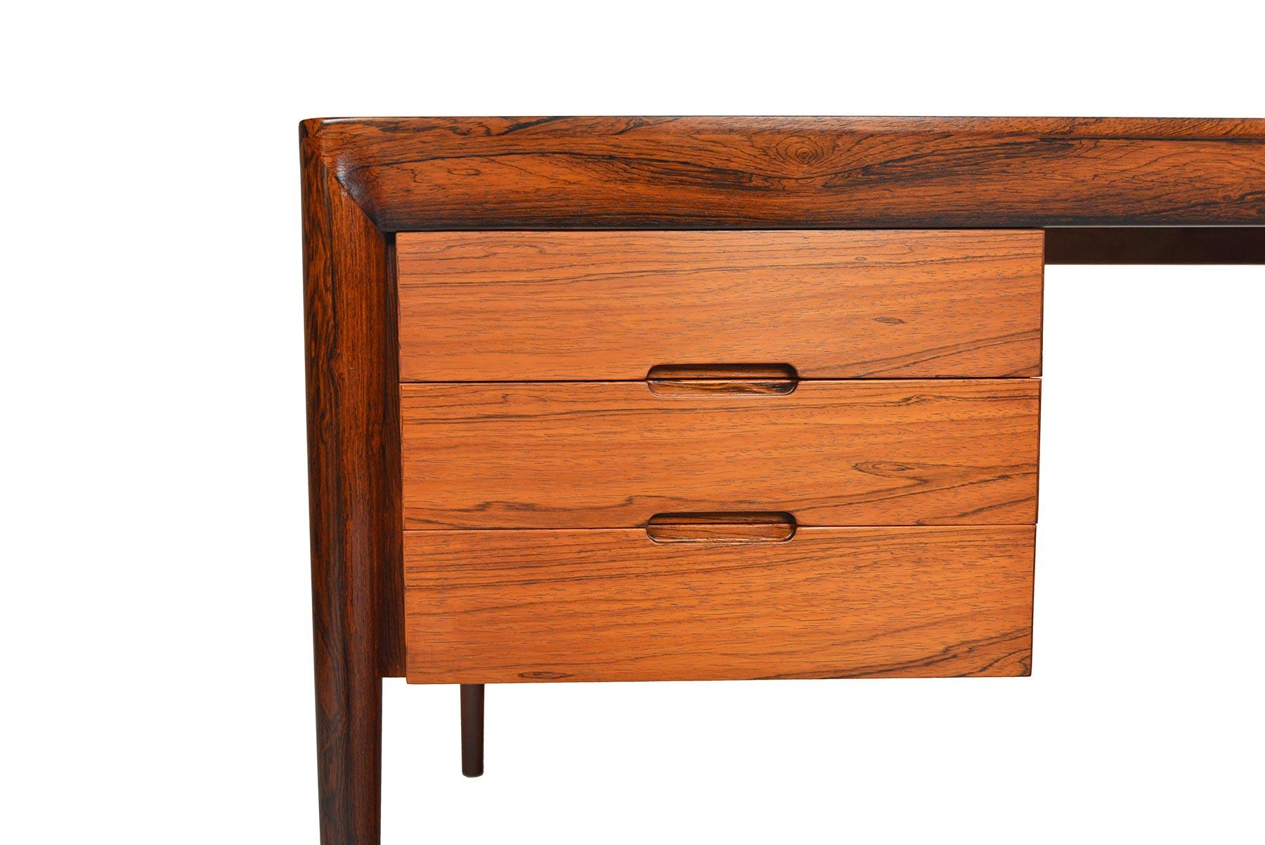 This rare Danish modern executive desk was designed by Erik Riisager Hansen for Haslev Møbelsnedkeri in the 1960s. The beautiful banding seamlessly joins to the exterior mounted legs. Crafted in Brazilian rosewood, the top slab features a raised lip