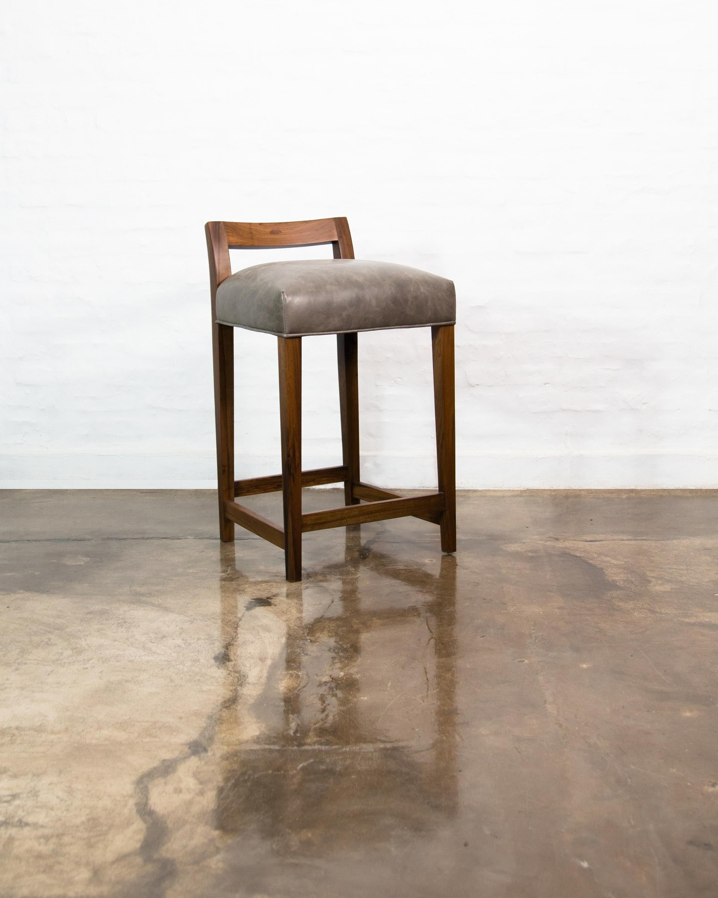 The Umberto counter stool is one of Costantini’s original seating designs, featuring a modern, low, carved solid wood back with a tight seat, and optional burnished bronze footrest. Available in several standard kinds of leather as well as COM/COL.