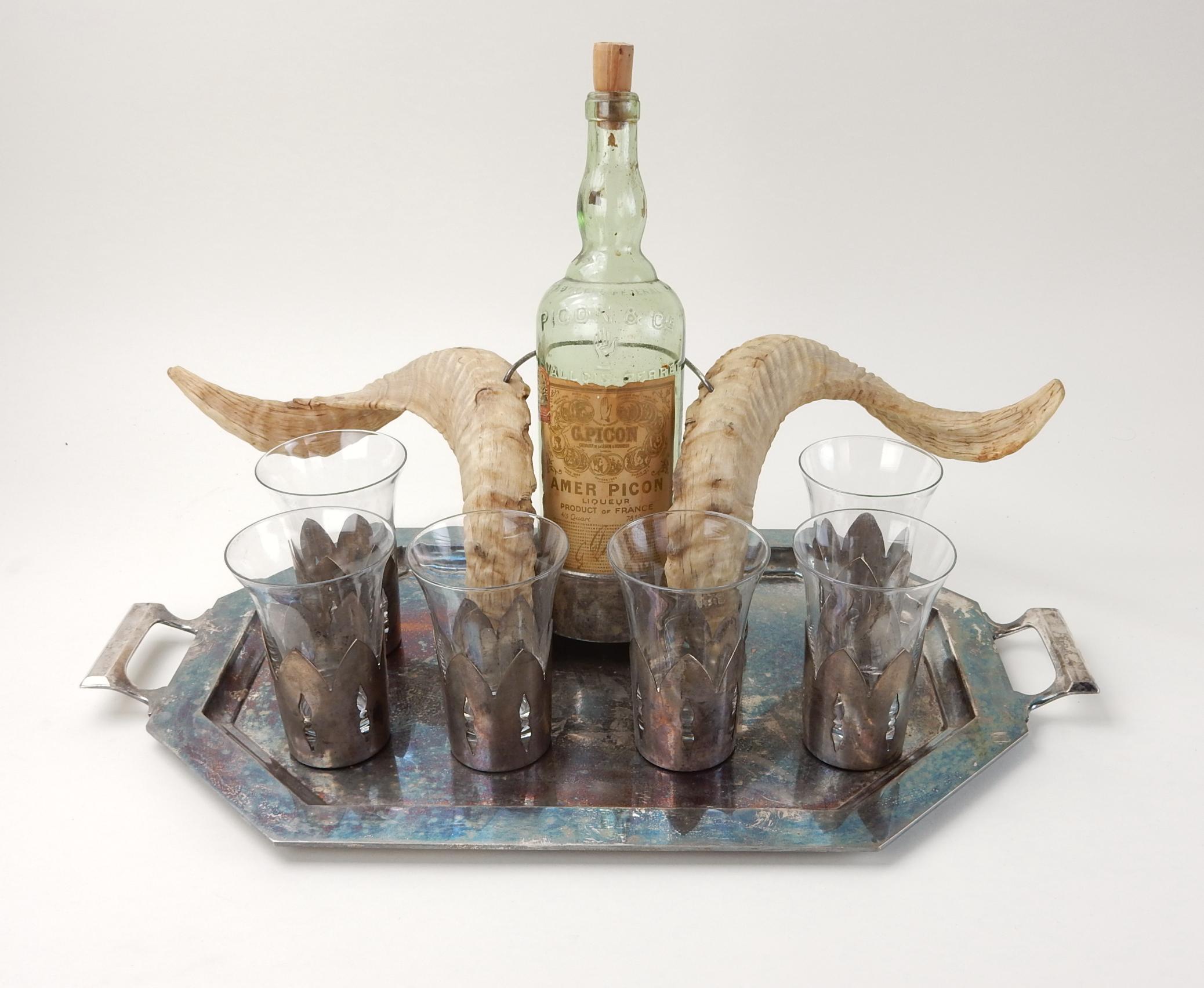 From a multi generational Basque family estate this remarkable bar set
consisting of exotic horn bottle/decanter holder, 6 glasses with pierced metal holders and a serving tray.
Present bottle, as found, being a French Picon, circa 1920s.
Unique