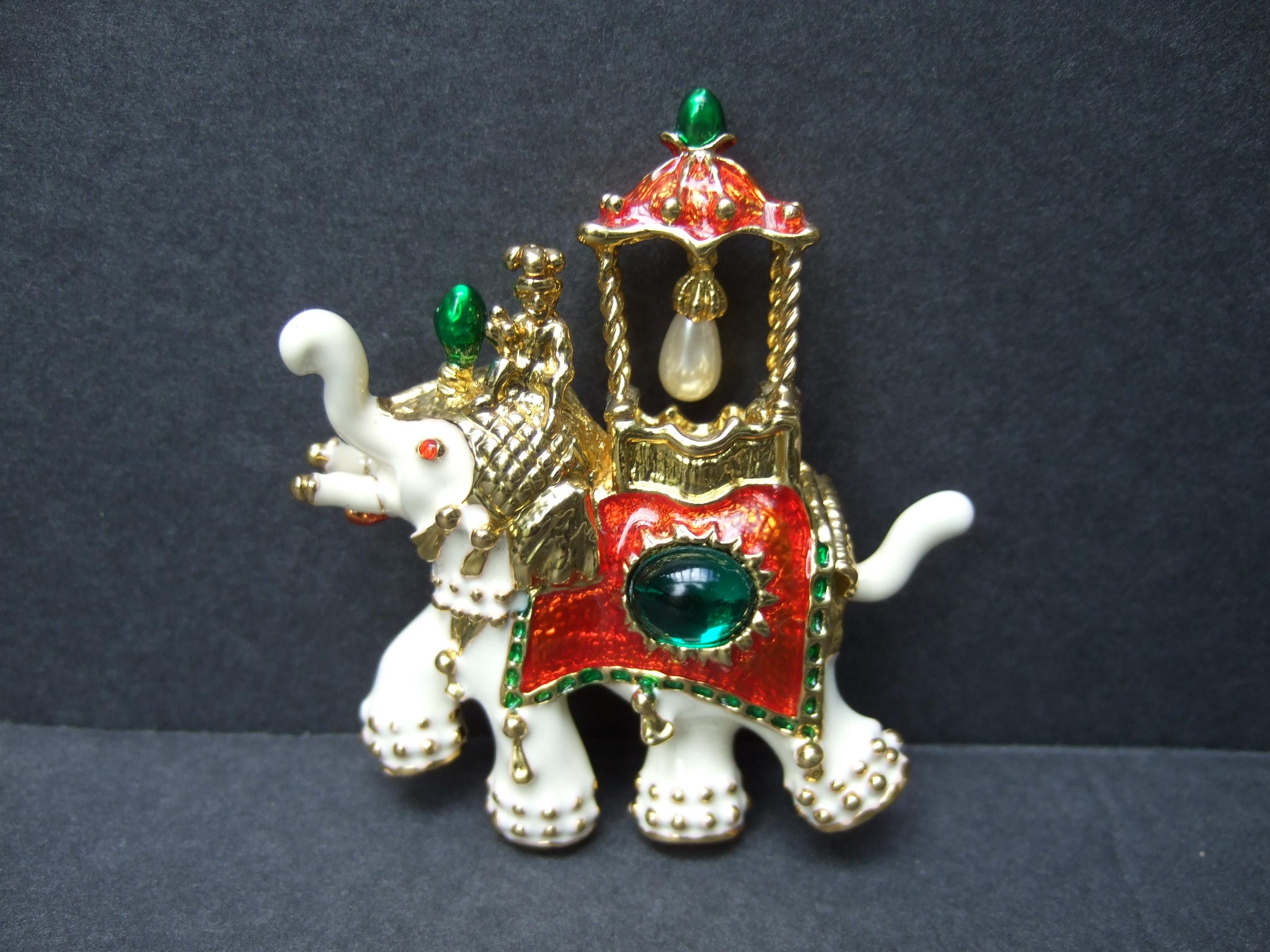 Exotic gilt metal jeweled enamel elephant brooch c 1990s
The unique gilt metal brooch is lacquered in creamy white enamel 
Adorned with an emerald green resin cabochon in the center
Accented with a tiny dangling resin enamel pearl 

A small gilt