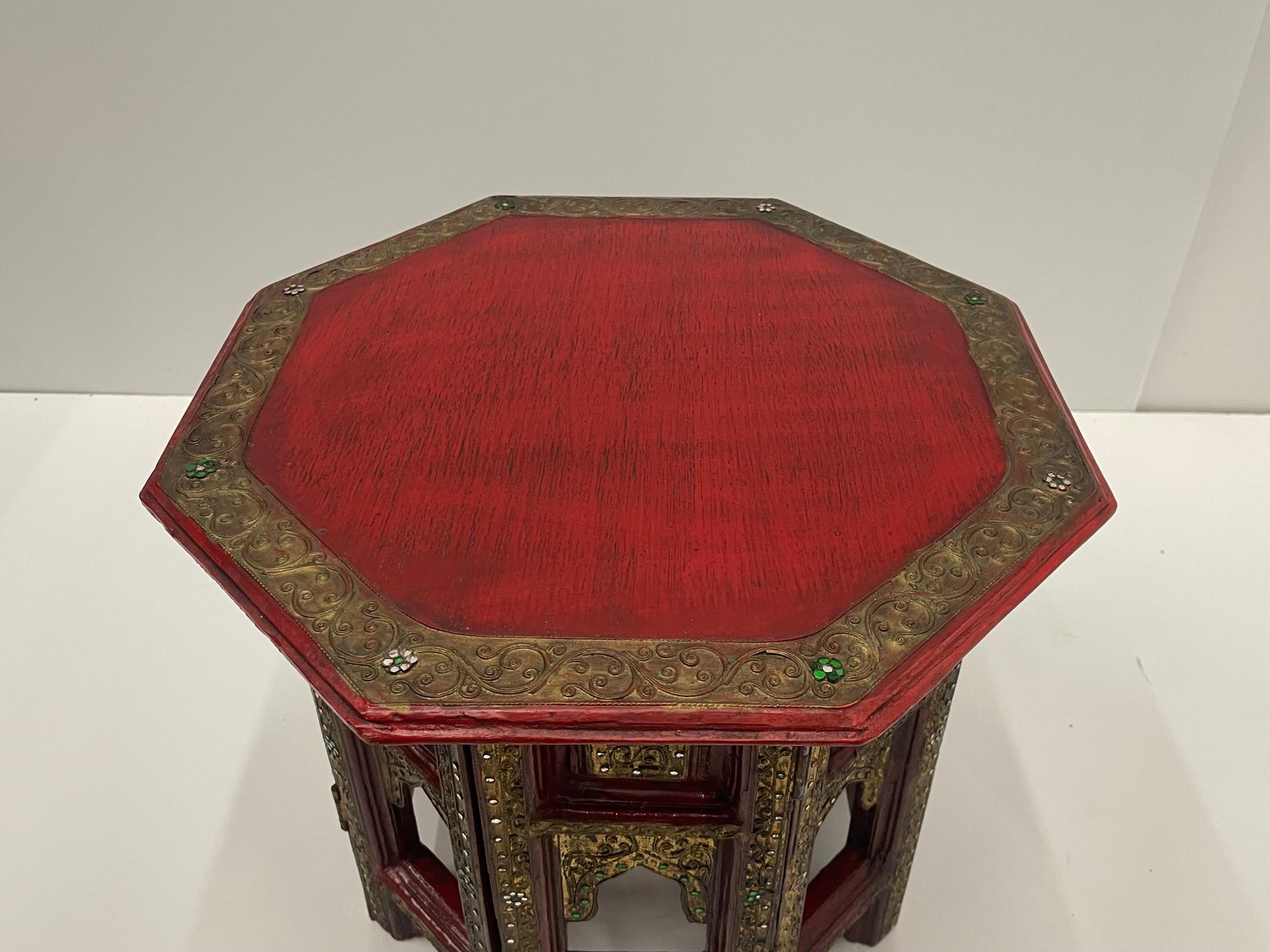 Striking and glamorous Moroccan side table having a red painted octagonal top, carved folding base embellished with glass inset beads, floral decoration and gilding.