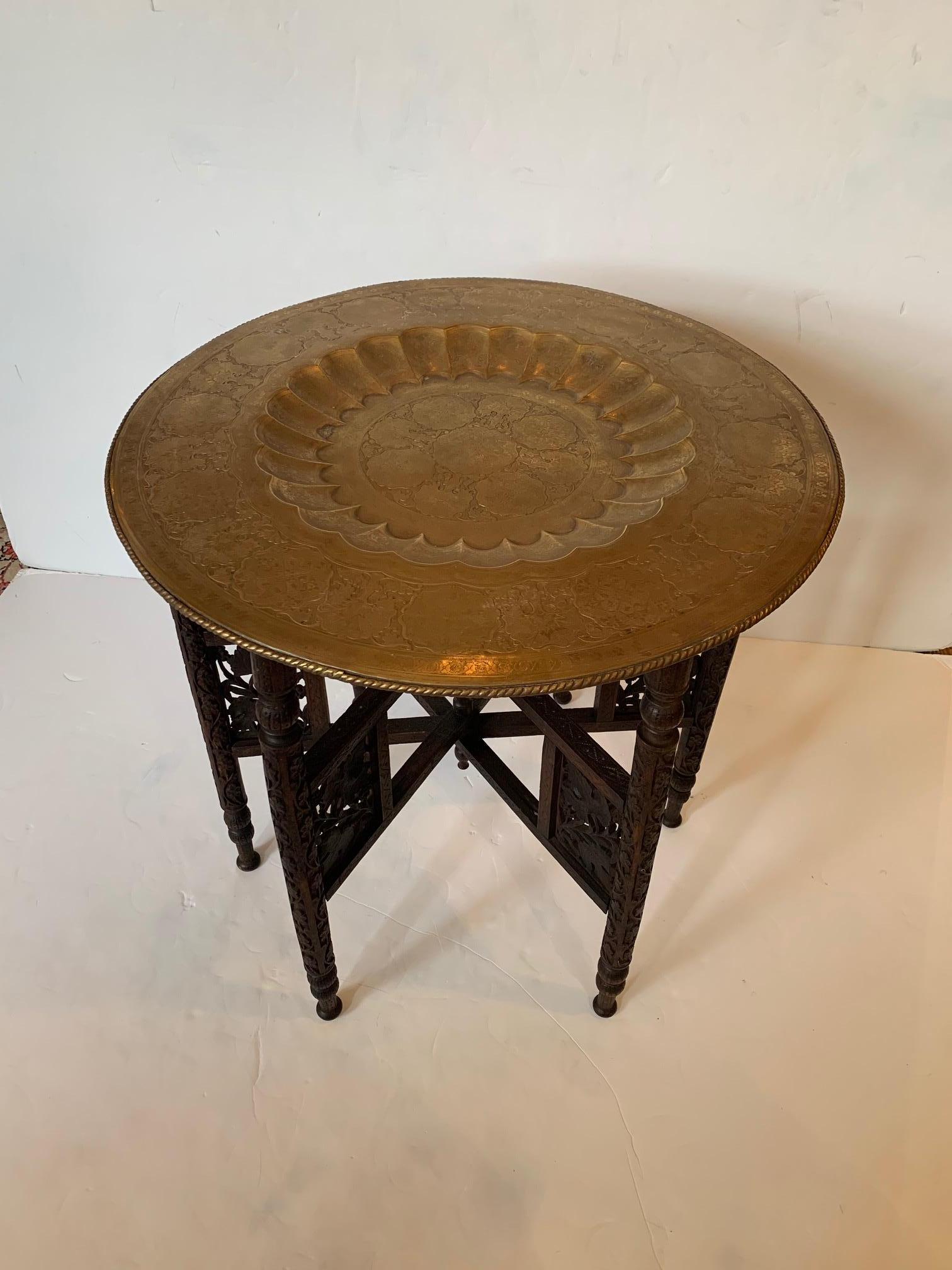 Exotic Moroccan tray top end table having beautiful etched brass tray with central recessed scalloped circle and folding intricately carved base. Brass has nice aged patina and matte finish.