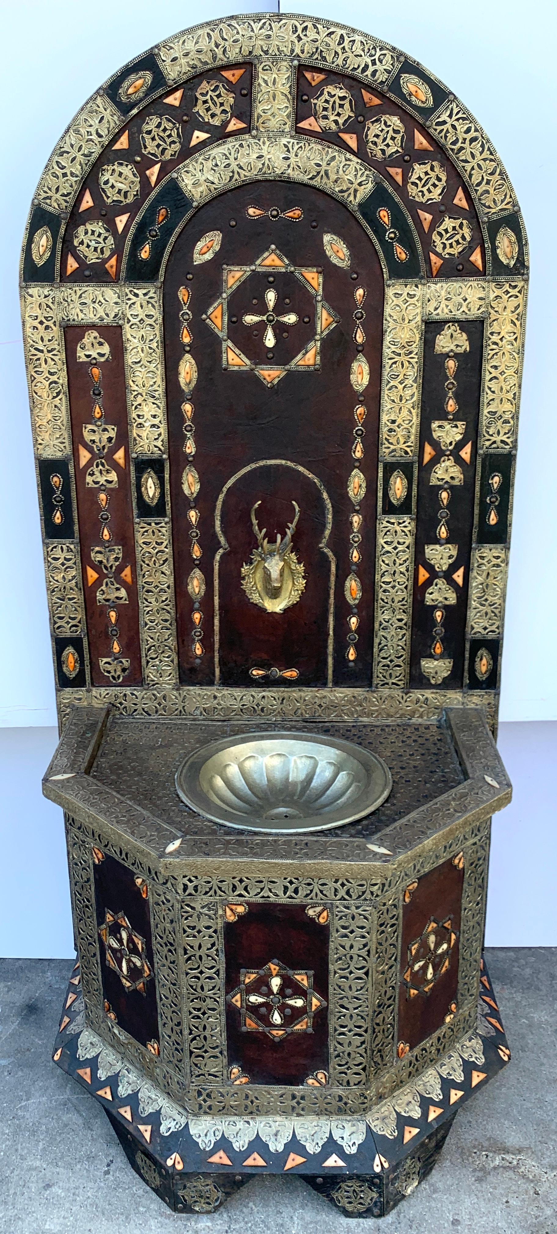 Exotic vintage Moroccan brass, bone, and silvered fountain, standing 6 feet tall the demilune backsplash profusely inlaid and mounted with various decorative elements, with a central brass stag fountain spilling into a 15-Inch diameter ribbed bowl