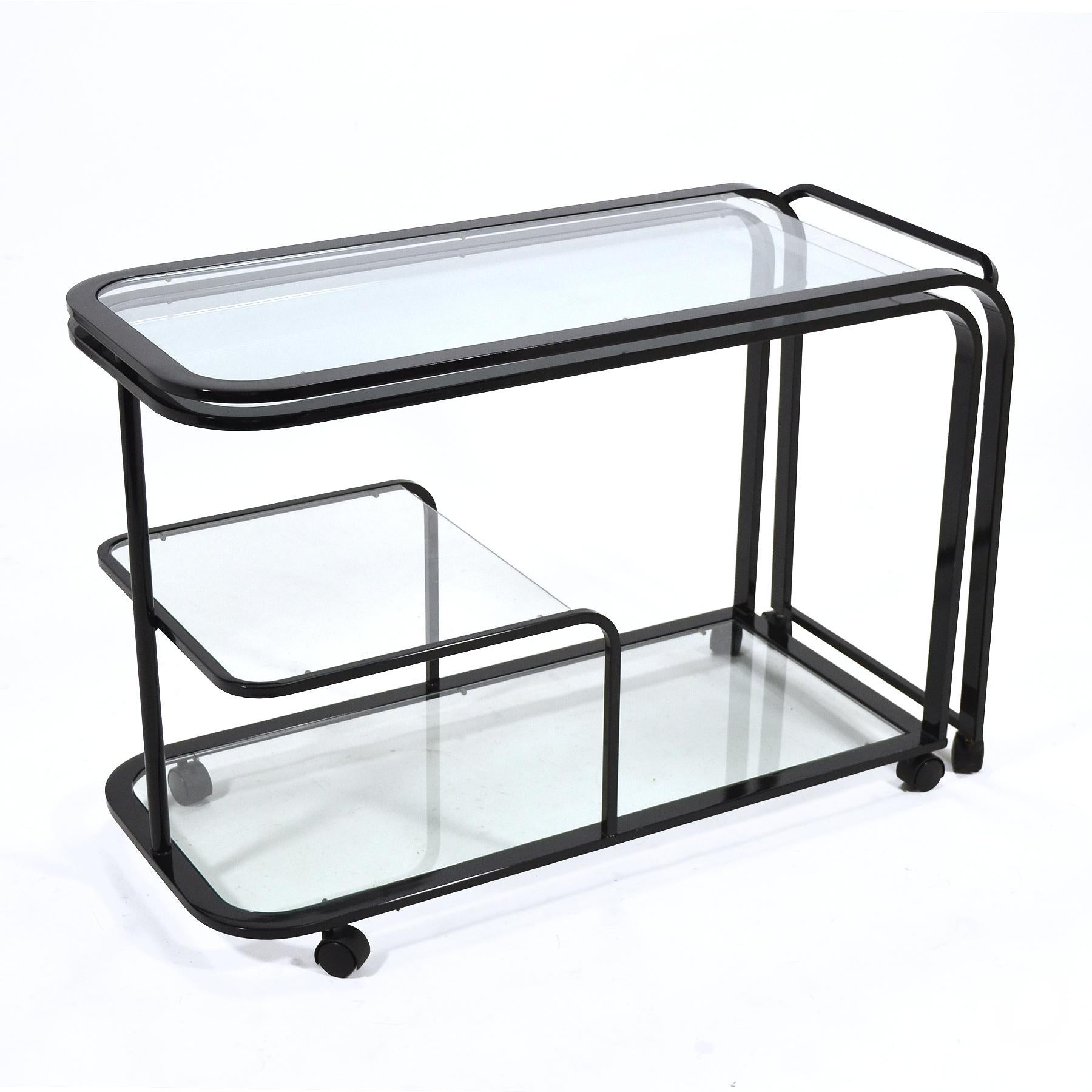 This great bar cart or serving cart by Design Institute of America can unlatch, swing open, and double in size to serve a large party. More commonly seen in brass or chrome, the black finish on the frame of this example lends a stronger graphic