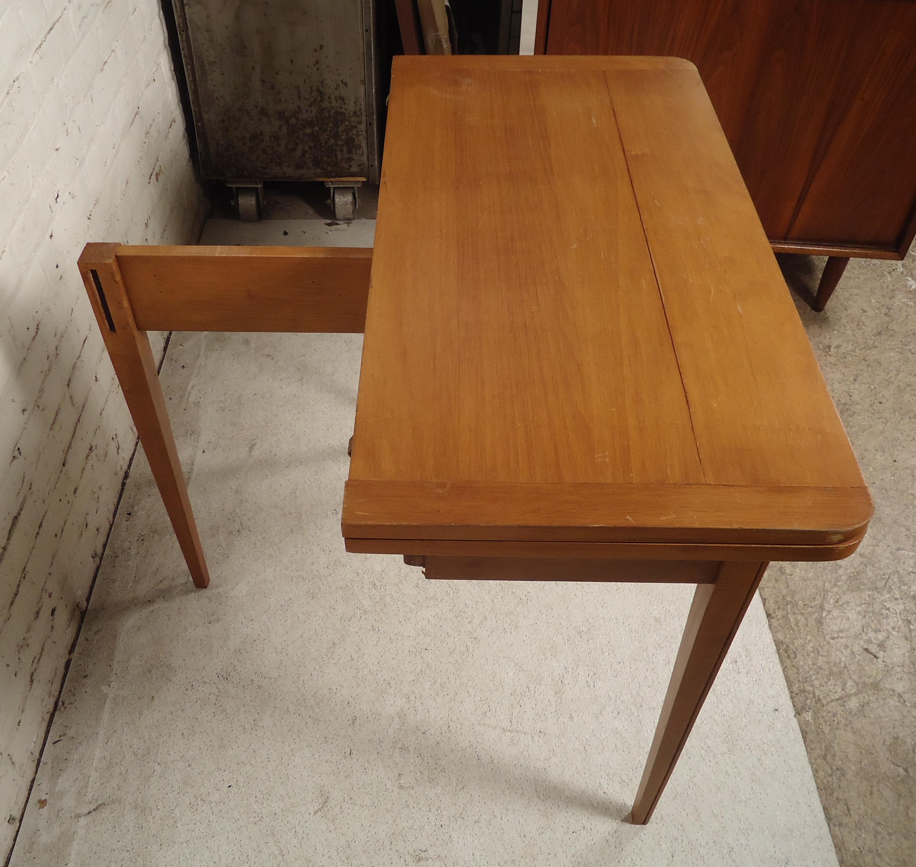 Sleek midcentury console table that opens to a square dining table. Maple grain with tapered legs. One leg swings out to support the table leaf.

(Please confirm item location - NY or NJ - with dealer).
 