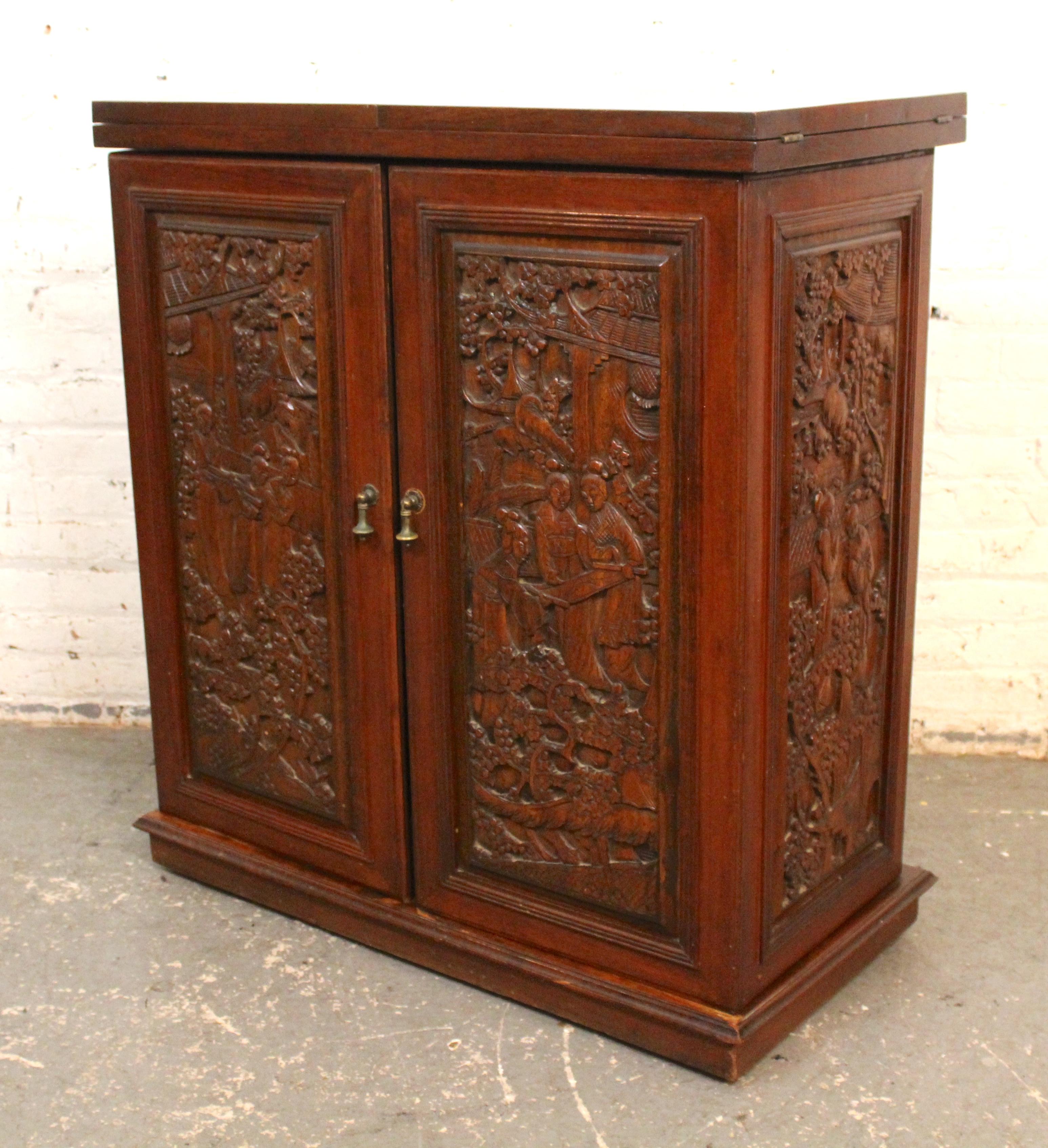This dry bar cabinet features an impressive hand carved front and side panels, plus three inset marble slabs on top. The cabinet has two doors that open and set underneath the fold out top, revealing ample bar storage, which includes drawers, bottle