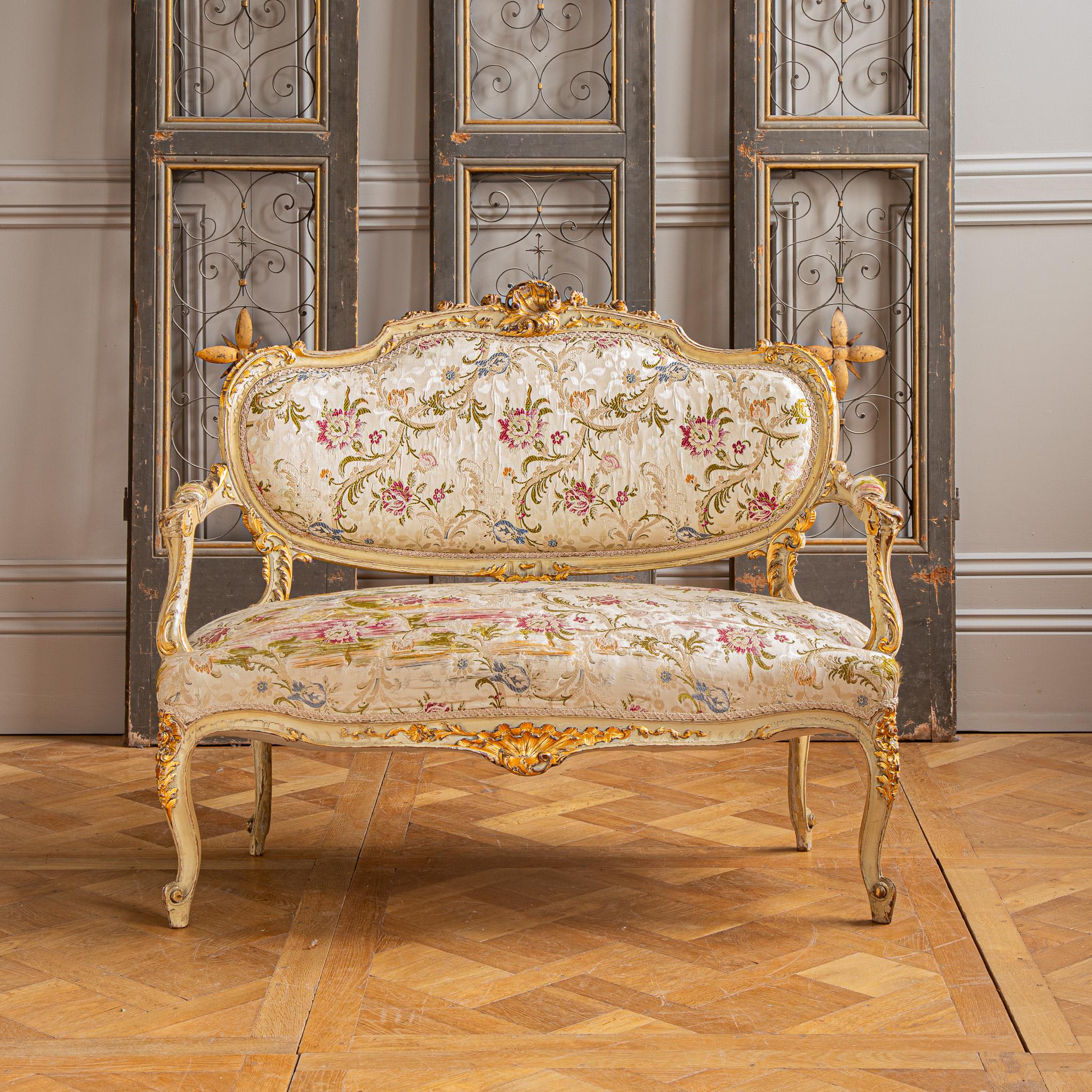A nine piece Italian, Louis XV style, gilt-wood Suite. This masterfully handcrafted set includes one sofa, two armchairs with matching footstools, and four chairs, all unified by a aged cream finish with elegant gold highlights, showcasing a