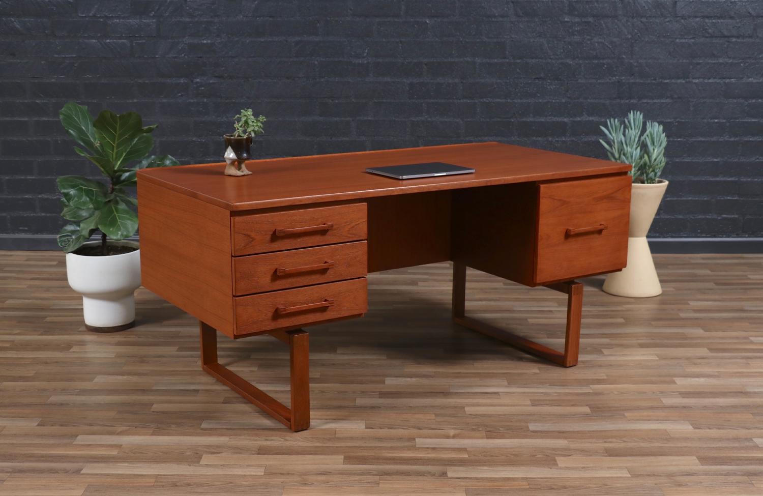 Designed by Henning Jensen and Torbin Valeur for Dyrlund, this stunning teak desk with an integrated bookcase exemplifies the best of Danish modern craftsmanship. The sleek, minimalist design features clean lines and a beautifully grained teak