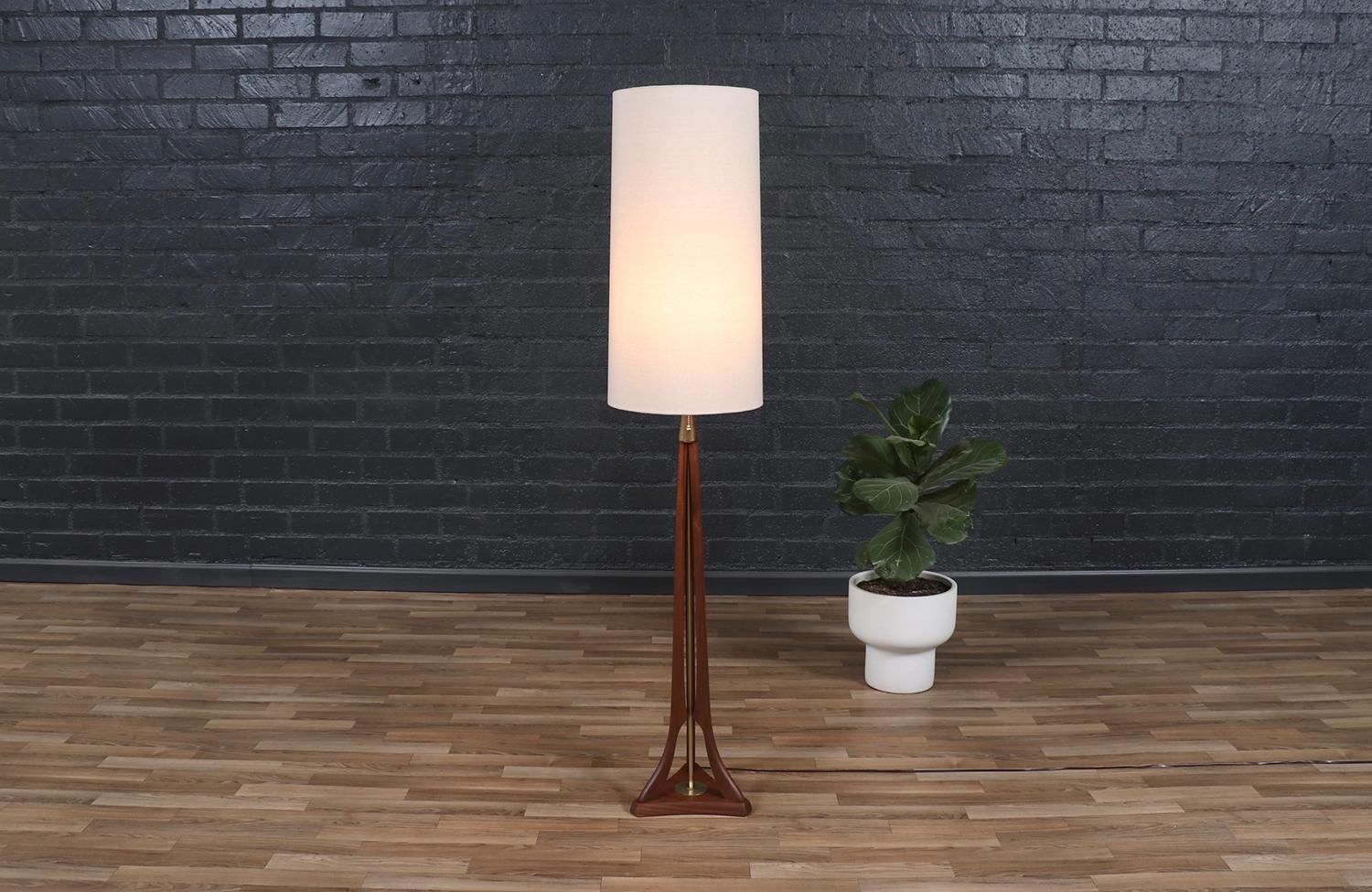 This striking floor lamp by Modeline of California showcases the perfect blend of sculptural elegance and functional design. Crafted from korina wood, its graceful three-legged base is accented with patinated brass details, providing a warm contrast