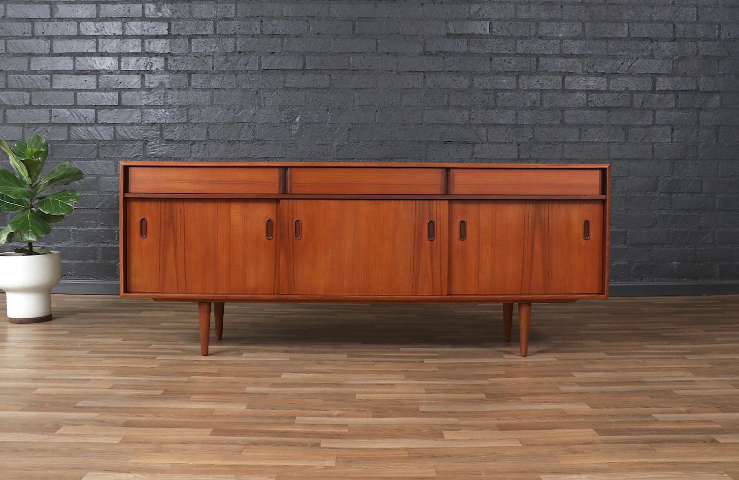 This exquisite Mid-Century Modern teak credenza, crafted by Punch Design in Canada during the 1960s, showcases timeless craftsmanship with a sleek and functional design. The sliding doors reveal spacious interior shelving, while the top drawers