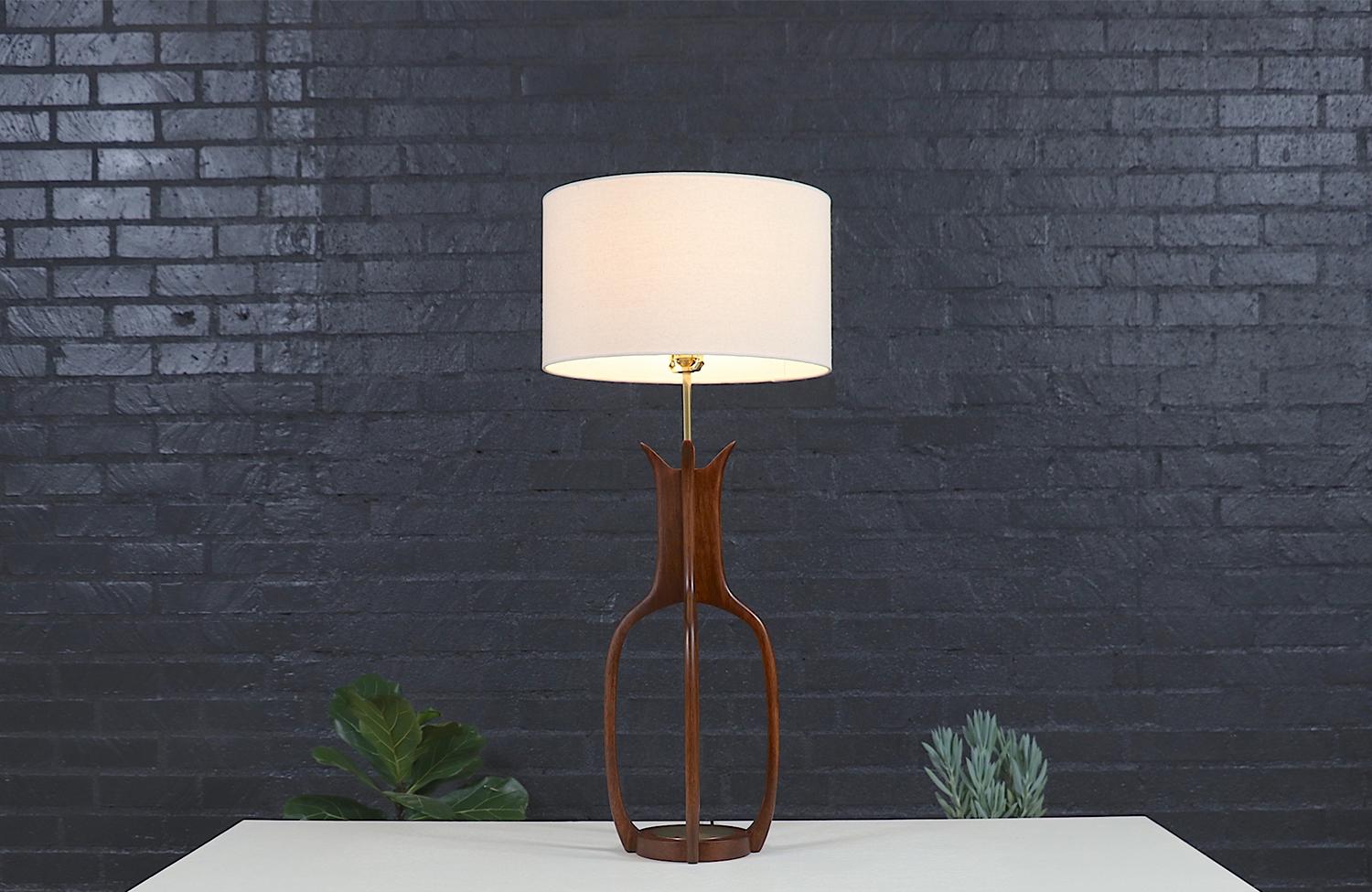 This striking table lamp by Modeline exemplifies mid-century modern artistry with its sculpted korina wood base and elegant, elongated form. The fluid curves and open design create a sense of movement, making it as much a sculptural statement as a
