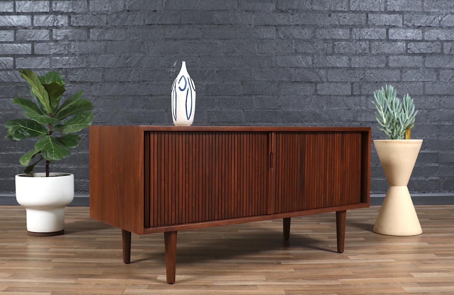 Mid-Century Modern low credenza designed by Milo Baughman for Glenn of California in the United States circa 1950s. This exceptional credenza features a sturdy walnut wood construction with four interior compartments, a set of tambour doors with