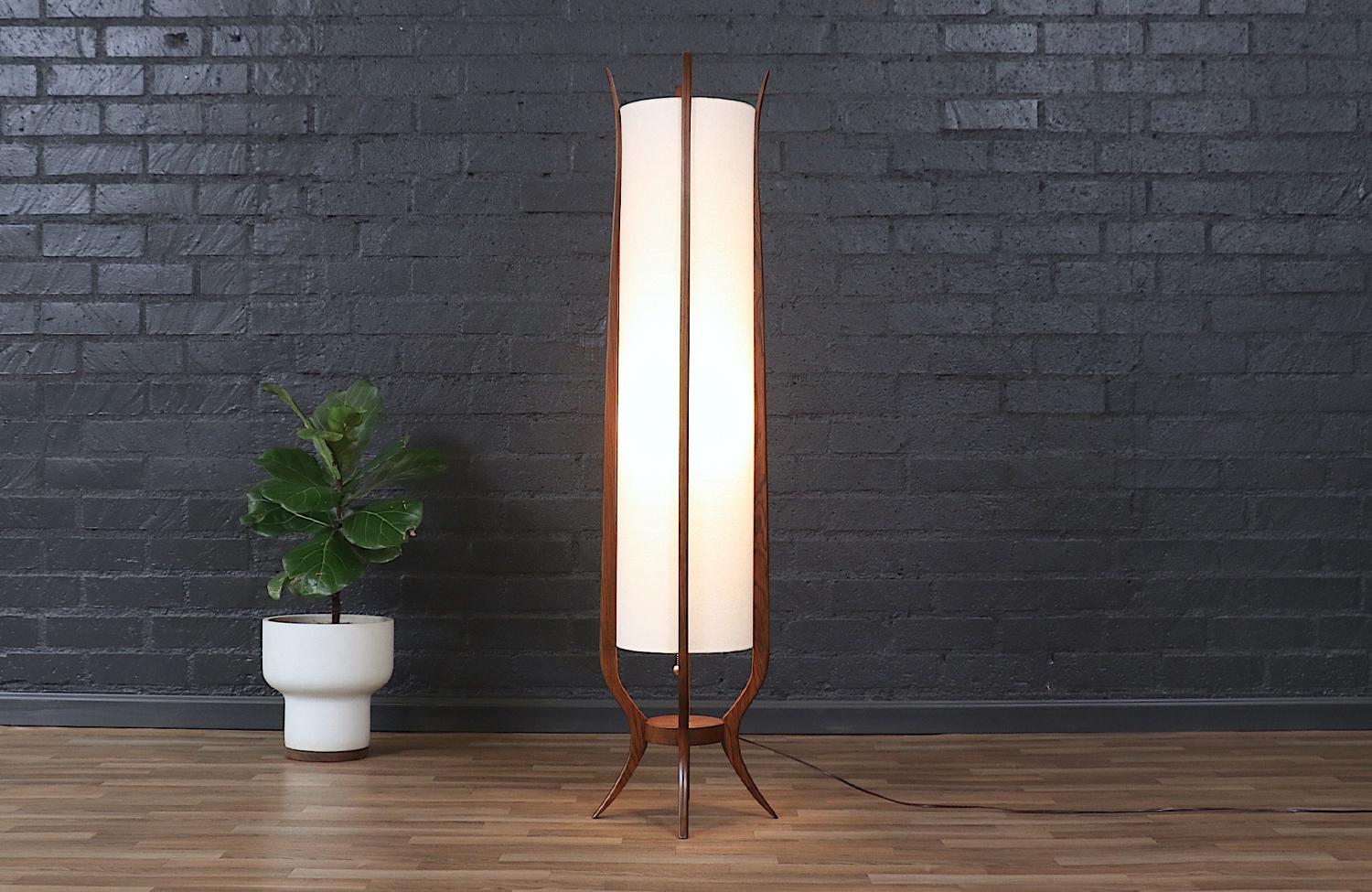 This sculptural Mid-Century Modern floor lamp by Roller Lamp Co. is a stunning statement piece with an elegant, organic form. The walnut-stained oak wood frame gracefully curves upward, embracing a custom linen shade that diffuses a warm, inviting