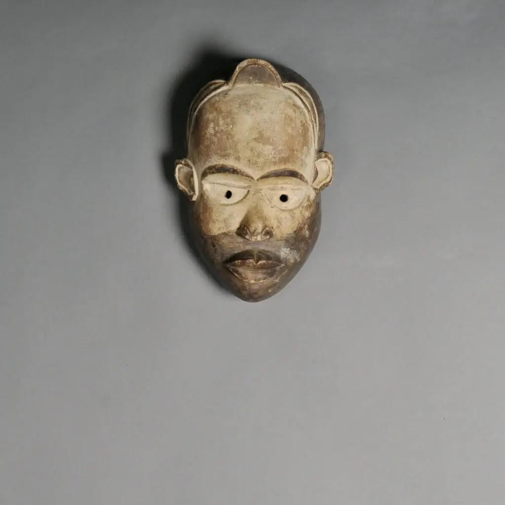 Diese authentische figürliche Kongo-Maske ist ein eindrucksvolles Beispiel afrikanischer Stammeskunst und wurde von Hand aus rohem, patiniertem Holz geschnitzt. Die Naturtöne, die von hellem Beige bis zu tiefem Braun reichen, betonen die