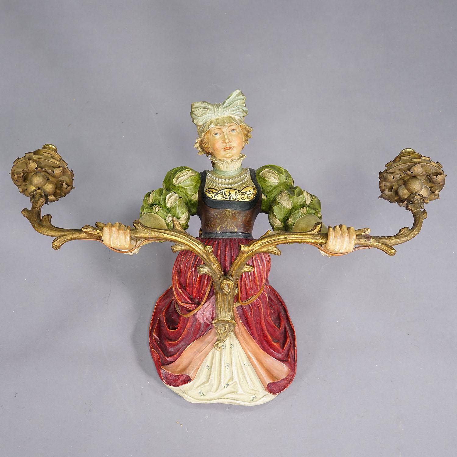 Applique de dame expressive en bois sculpté, vers 1900

Une applique murale ancienne avec une statue sculptée à la main d'une dame victorienne tenant un chandelier à deux faces. Réalisée en Allemagne vers 1900, elle est faite de bois et de stuc et