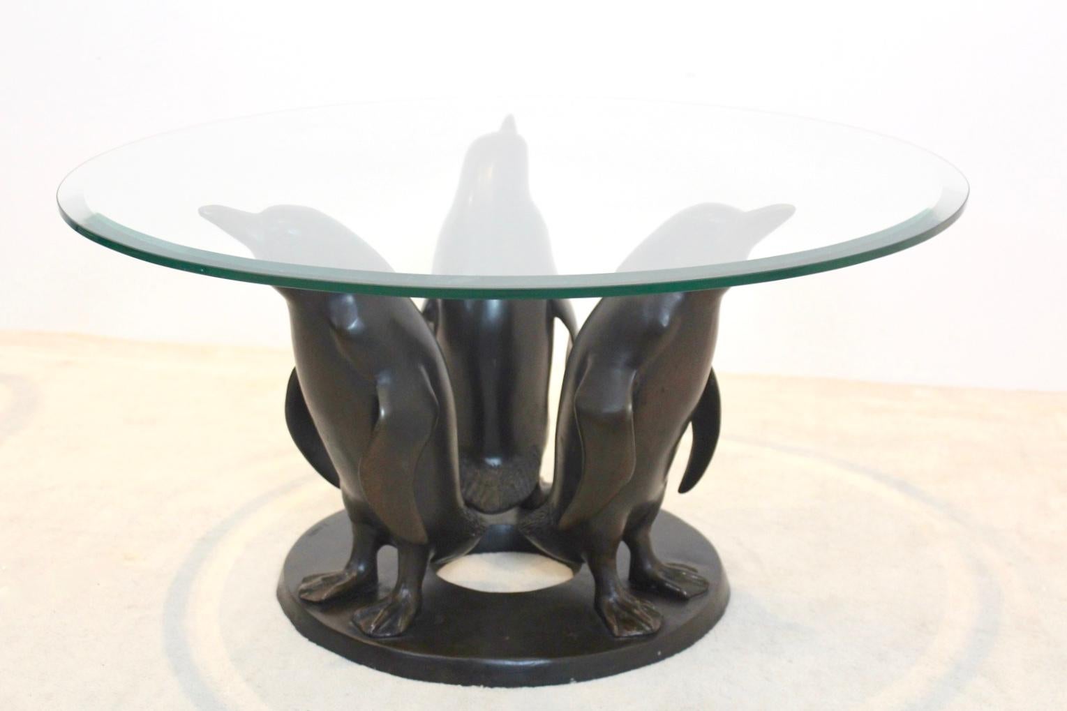 A truly eye-catching original bronze penguin coffee table designed by J. Daste. A heavy Bronze base with a solid (facet) glass top. The base comes with a beautifull patina with three penguins holding the glass top. Signed by J. Daste on the base.