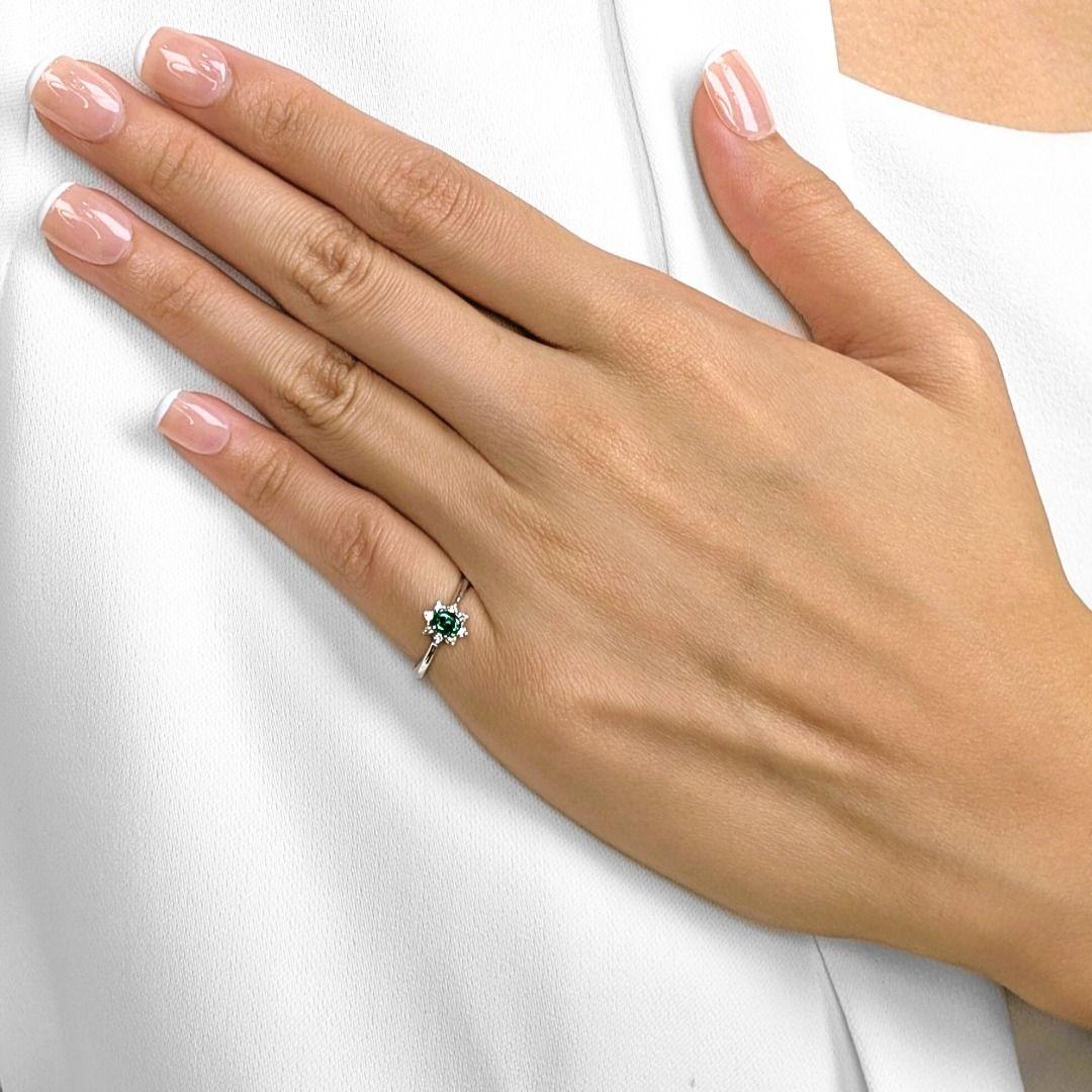 Questo delicato anello è una celebrazione dell'eleganza senza tempo, incentrata su un vivido smeraldo verde ovale da 0,11 ct che risplende di fascino naturale. Intorno allo smeraldo, 8 diamanti tondi brillanti naturali (0,04 carati in totale, colore