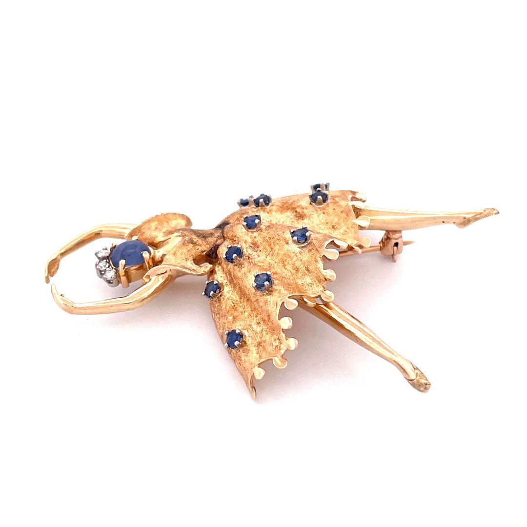 Adorn yourself with elegance and grace with our 14k yellow gold sapphire ballerina brooch. This stunning brooch features an oval-shaped sapphire face, adorning her skirts are ten shimmering sapphires and the brooch is crowned with three dazzling