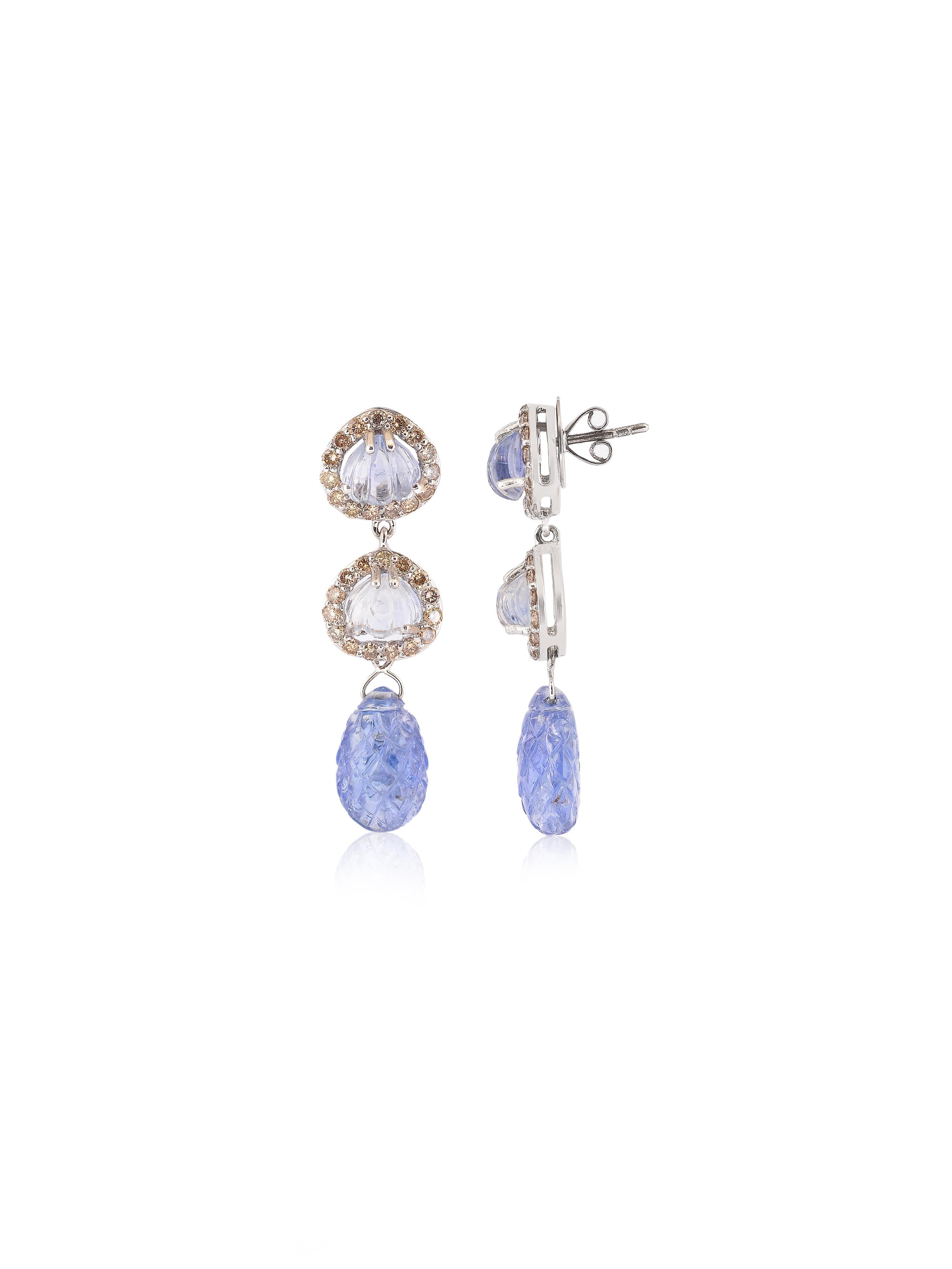 A pair of beautiful earrings with a hand carved natural sapphire drop pair weighing 16.49 carats along with 2 more shell shaped lighter sapphires on top surrounded by a halo of diamonds. 
The elegant dangling earring pair is made in 18K White gold.