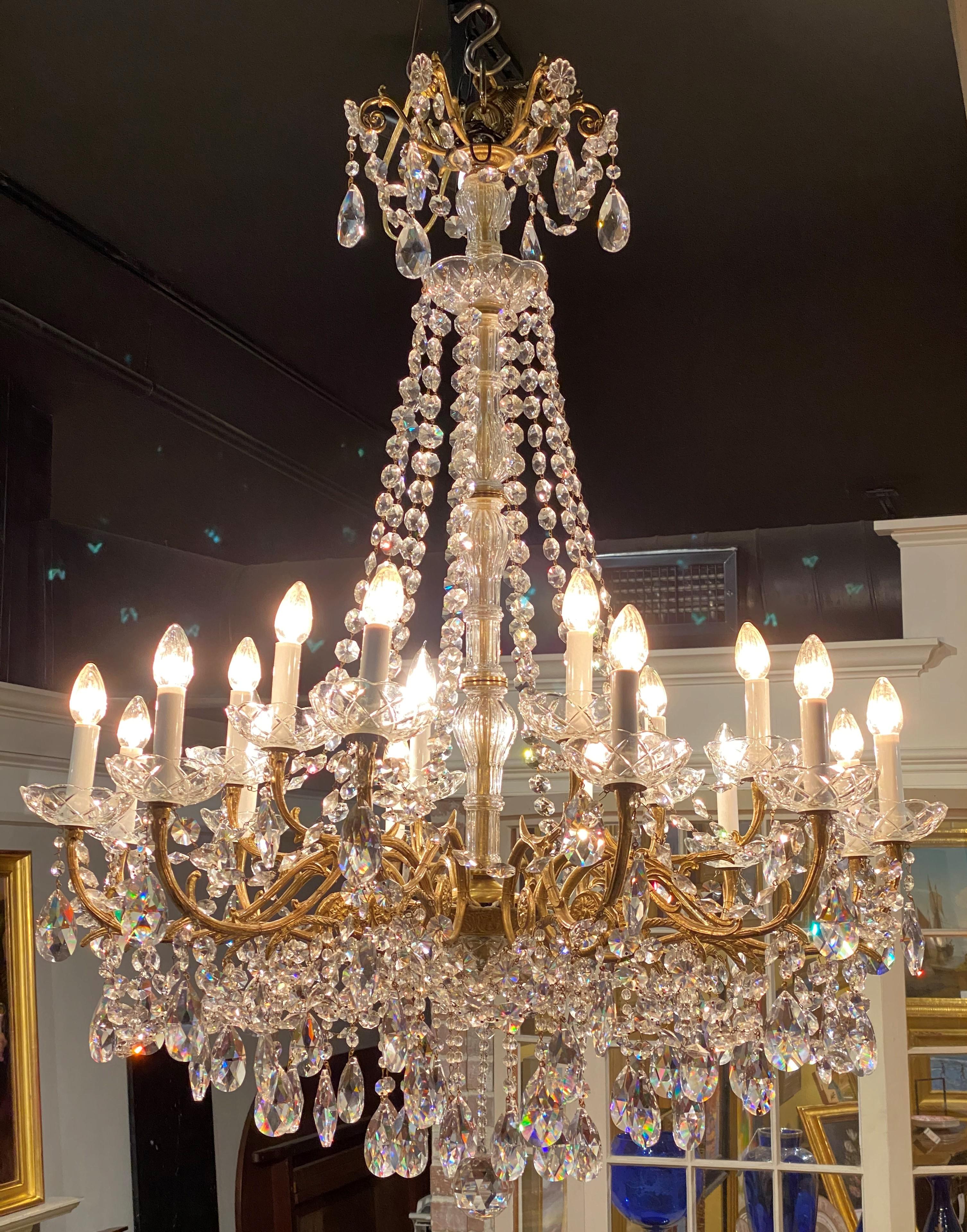 An exquisite French style tiered 18 light chandelier (12 lower, 6 upper) with a crown form crest with floral prisms, surmounting flowing strung prisms around a center crystal column down to brass S scroll arms terminating with candle lights, along