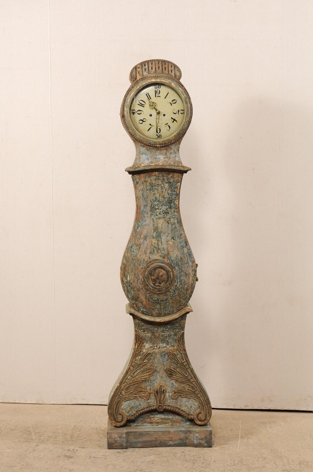 A 19th century painted wood Swedish long-case clock with distinct curvy rain-drop shaped belly. This antique floor clock from Sweden has an elongated arch crest atop it's head, with carvings and trimmed accents about it's edges and repeated about